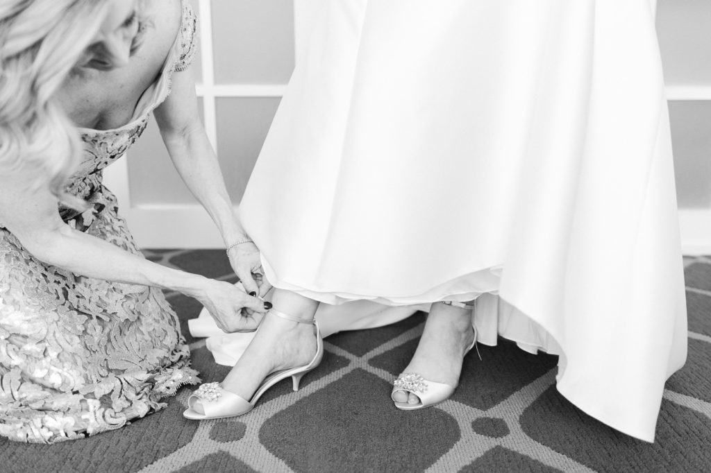 bride getting ready in hotel commonwealth with her mom helping her | sleek mermaid fit and flare dress | Badgley Mischka wedding shoes | black and white