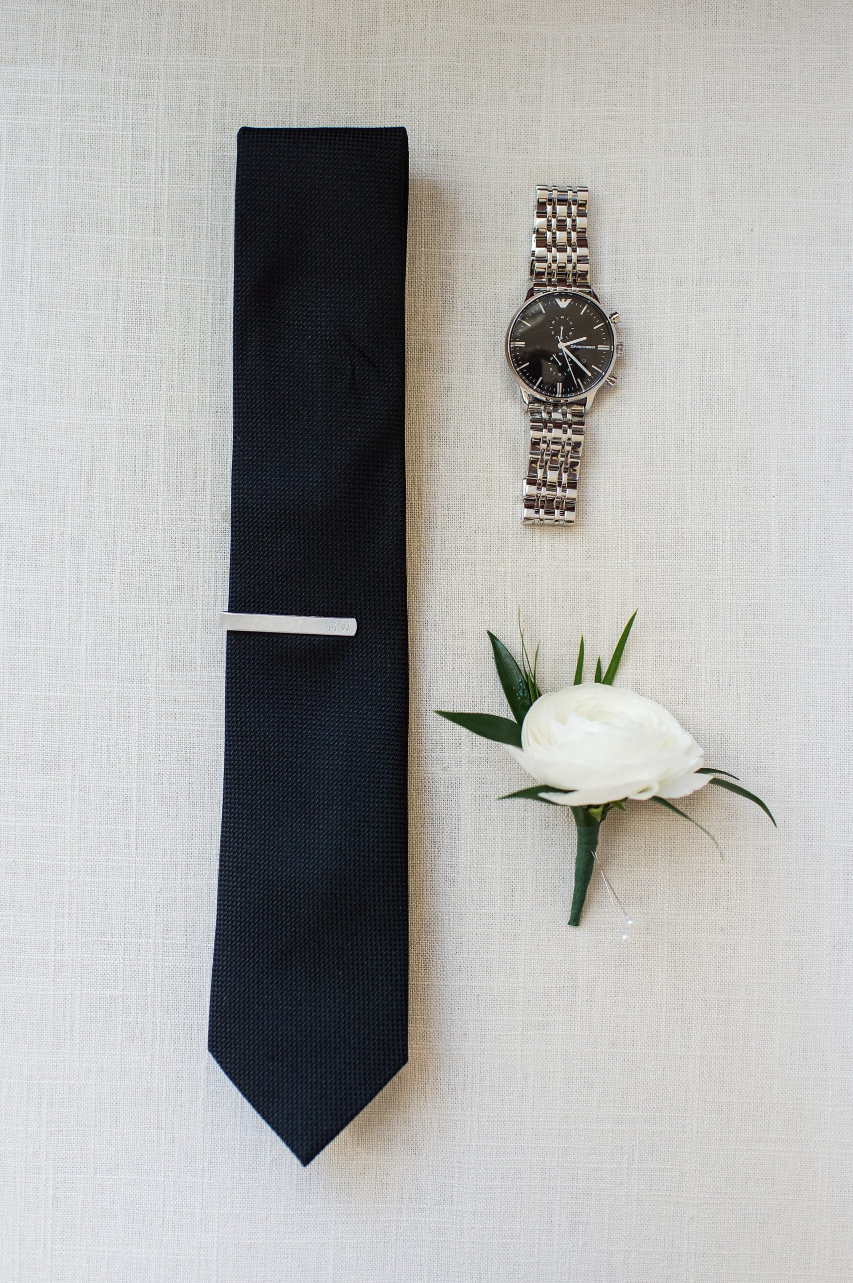 grooms details in styled flat lay with tie watch and boutonniere