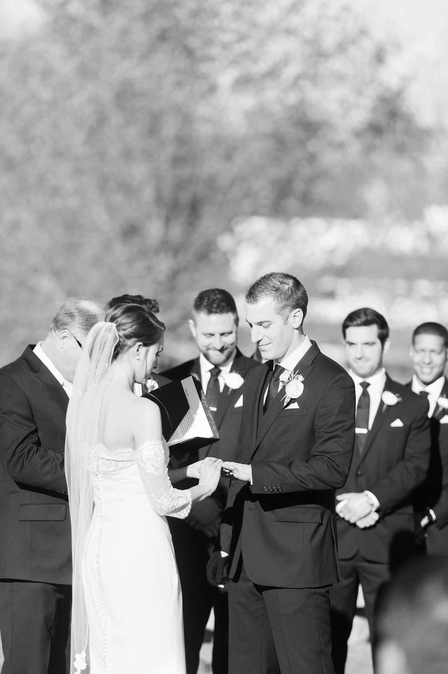 Black and white of bride and groom exchanging rings in outdoor ceremony