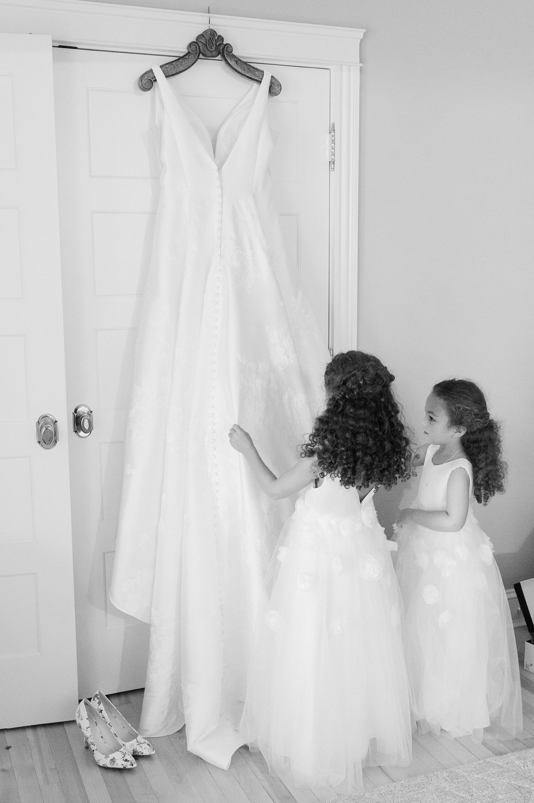 black and white photo of flower girls looking at the brides wedding dress hung up