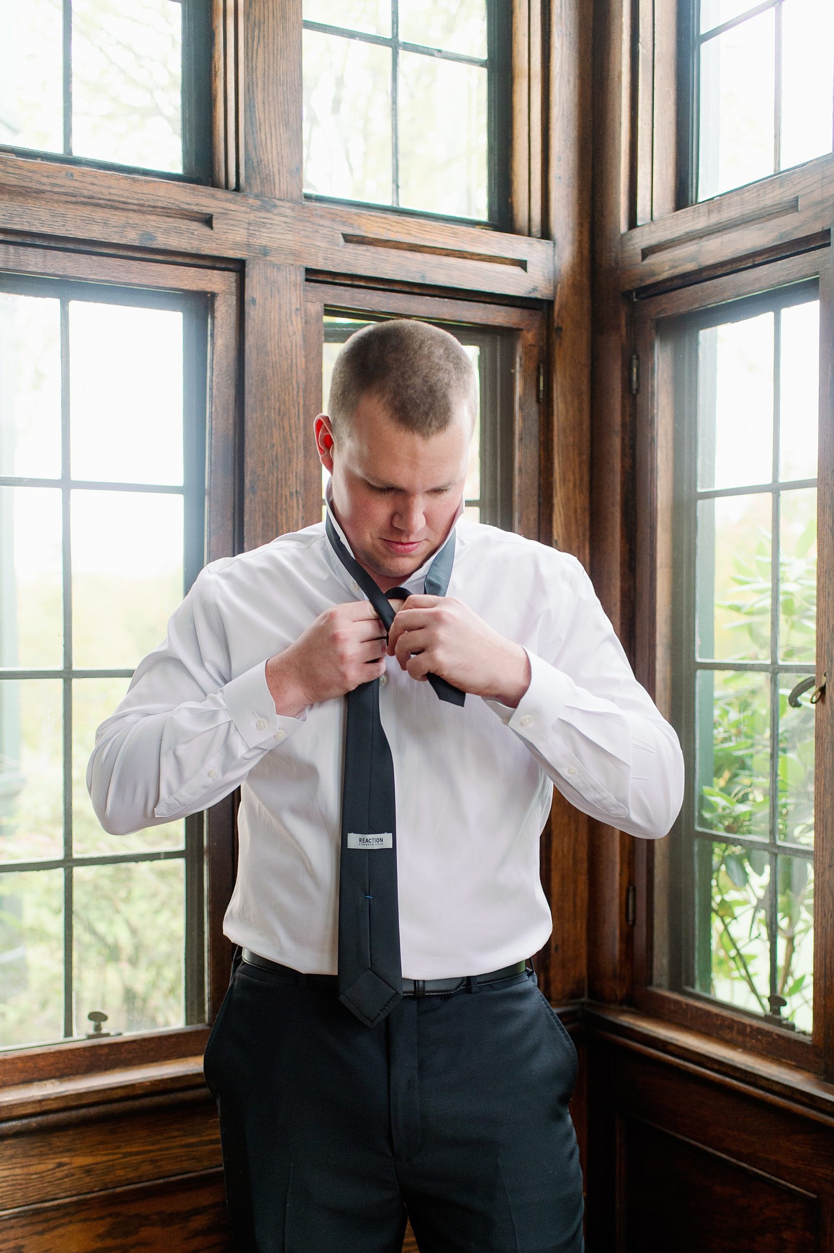 Groom ties his tie as he gets ready for his The Stone Barn Wedding in Maine