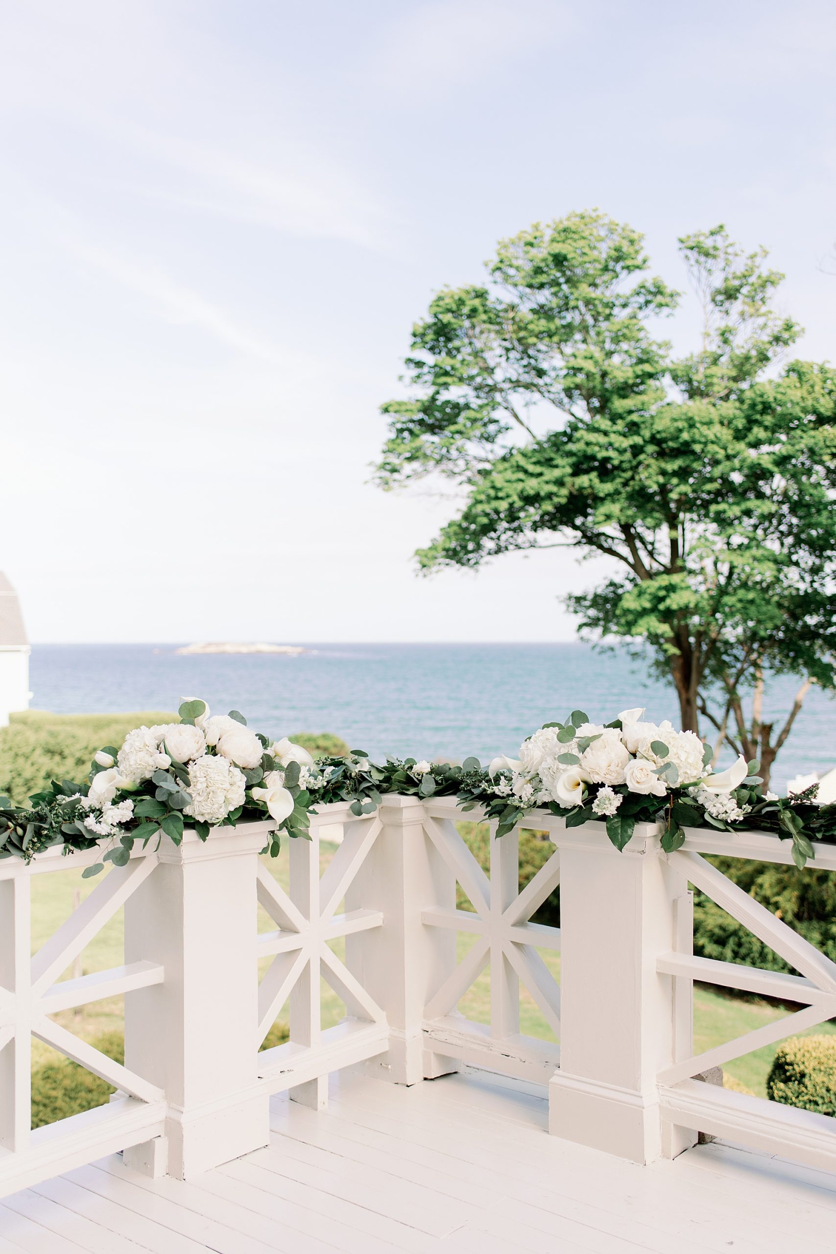 whites and greenery wedding ceremony backdrop flowers on railing of deck with view of water
