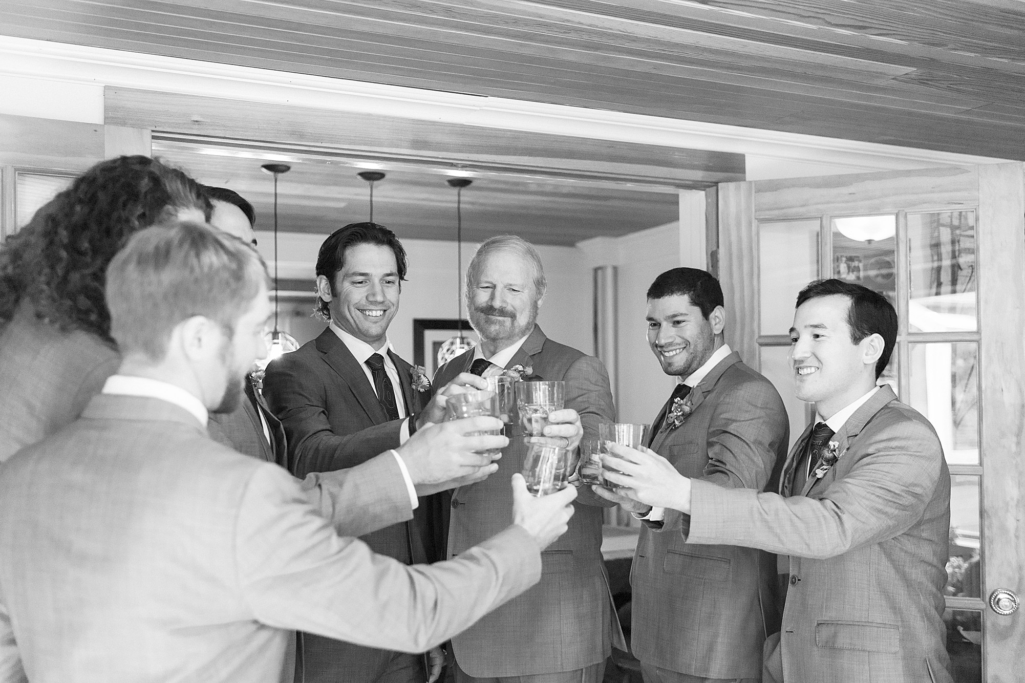 black and white of groom and groomsmen toasting before adirondack wedding at The Bark Eater Inn