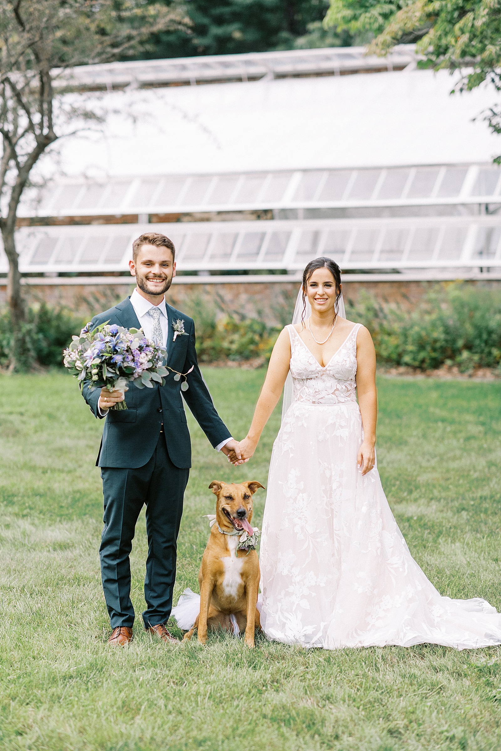 Bride and groom holding hands over their puppy, all decked out for the wedding. 