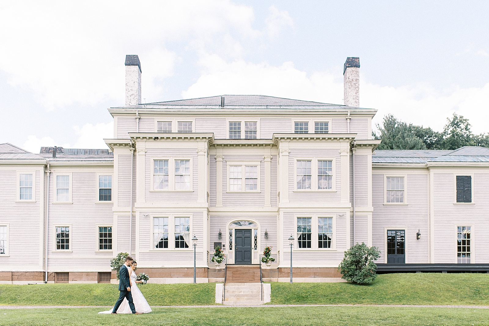 Bride and groom walking across the lawn in front of The Lyman Estate in New York. 