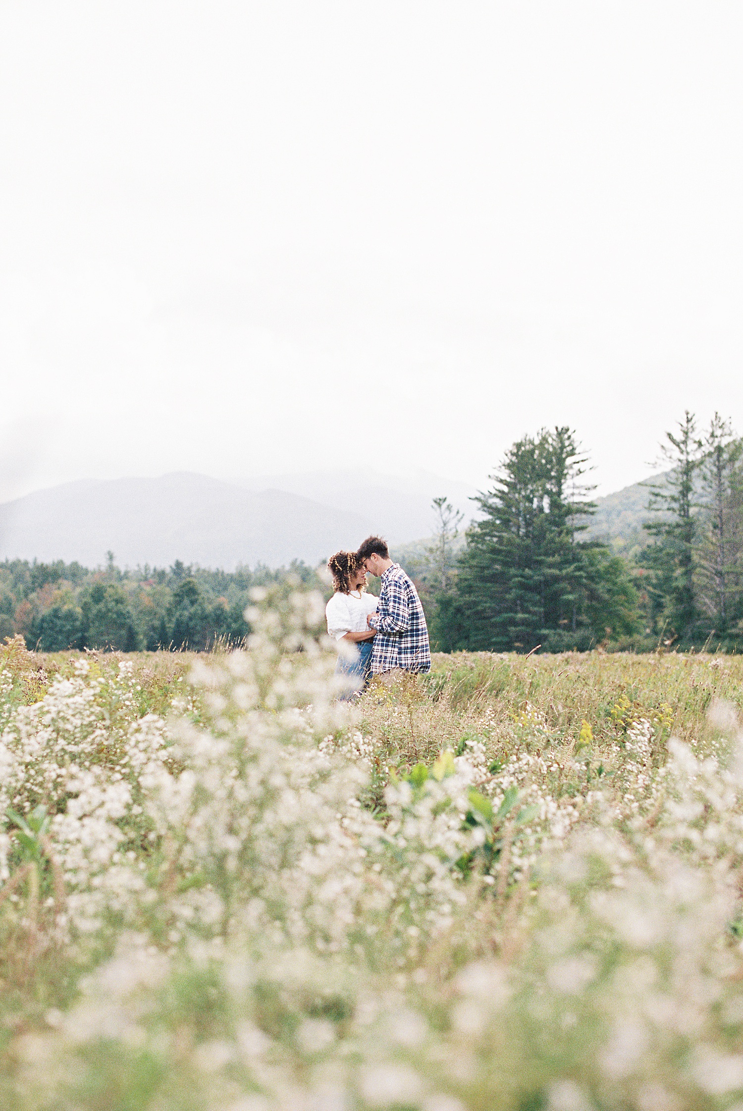 Man and woman embracing in a field of flowers with the foggy mountains in the background for their portrait photo shoot. 