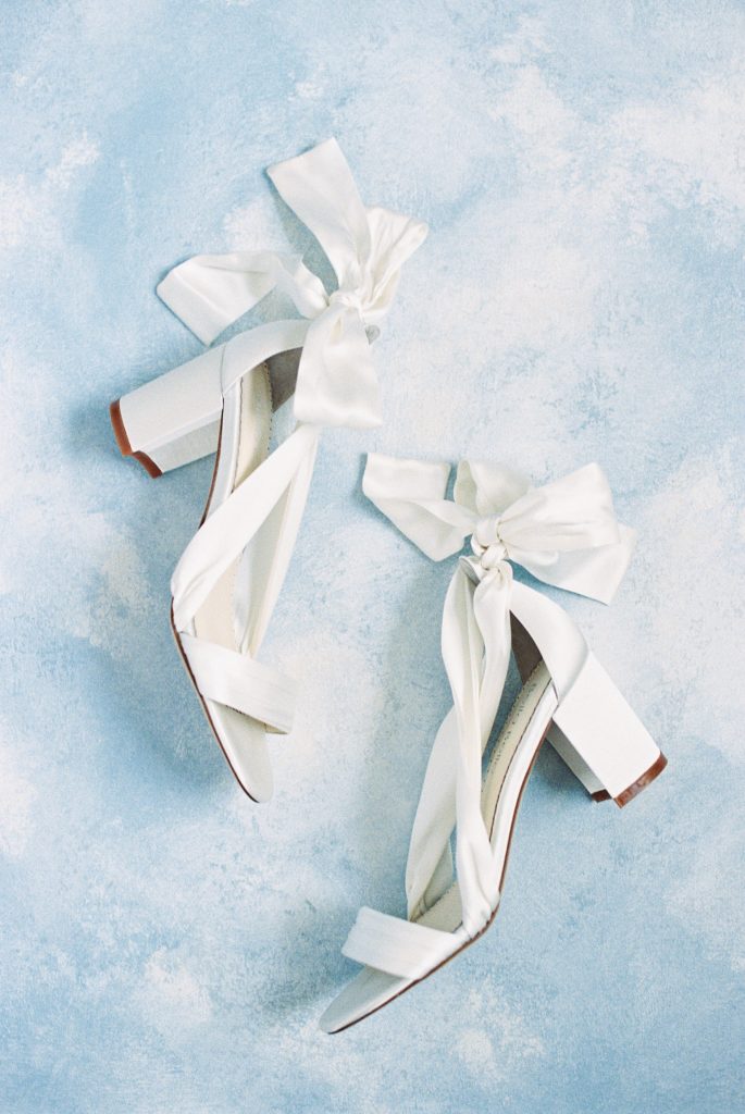 White wedding shoes on a blue background for blog post about streamlining your workflow for wedding creatives. 