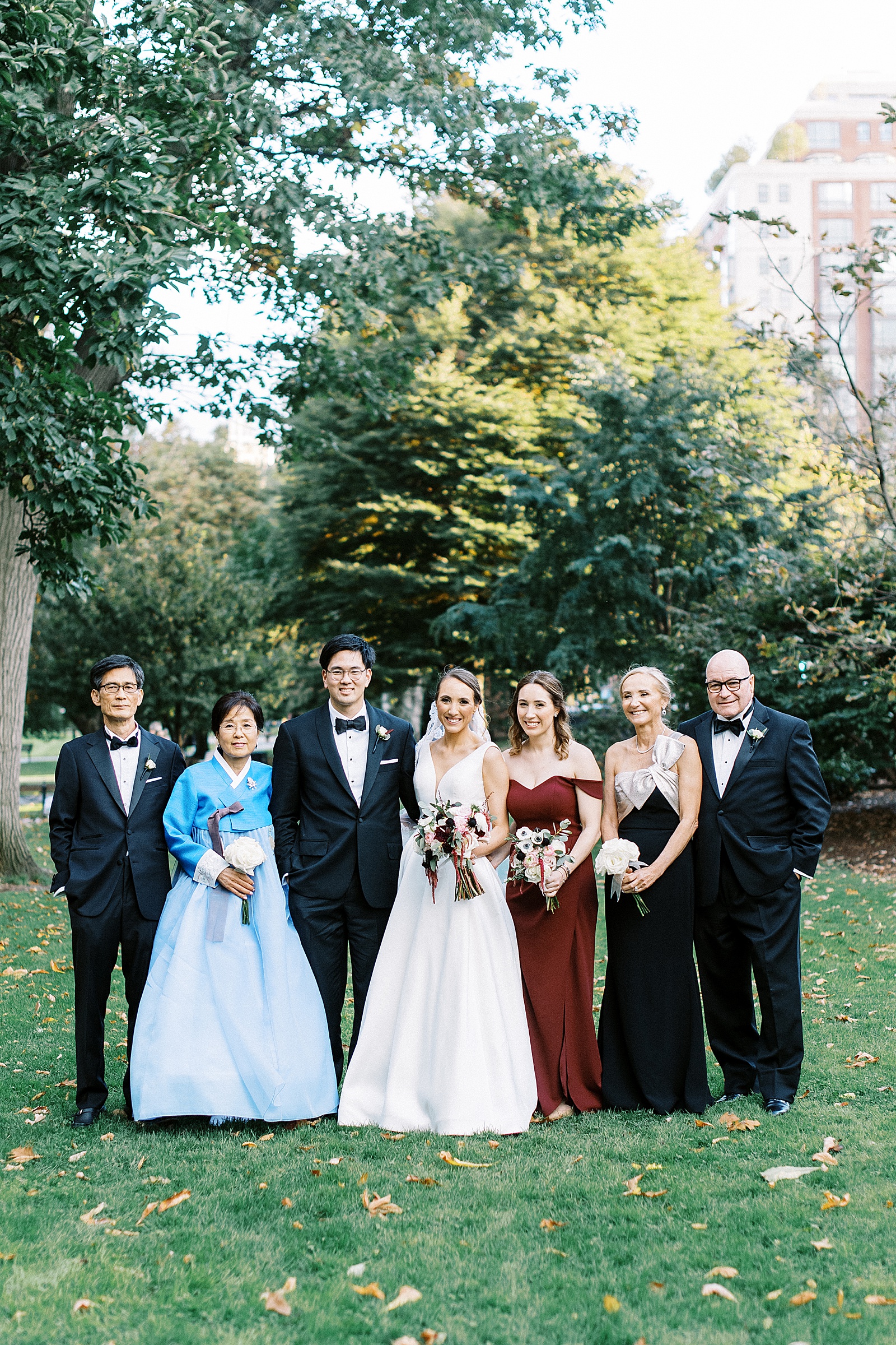 Bride and groom stand with their whole family in formal wear in a park after their wedding. 