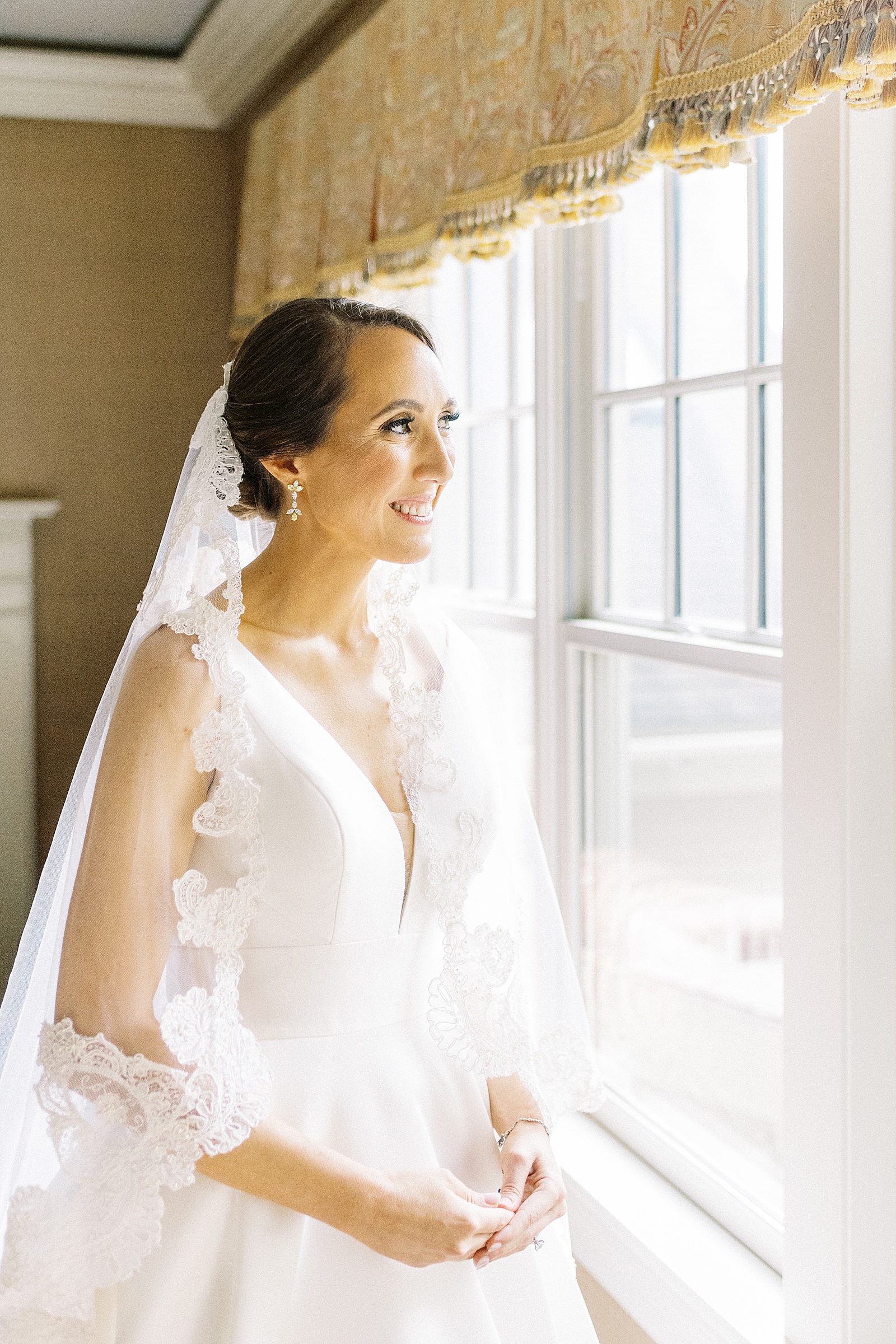 Bride with lace veil looking out a window before her Mandarin Boston Wedding.