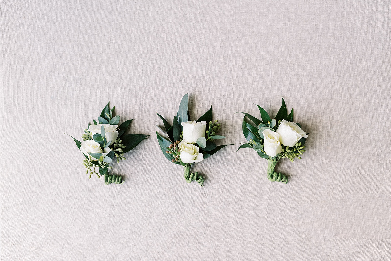 Three white rose boutonnieres for a New York wedding on a canvas background. 