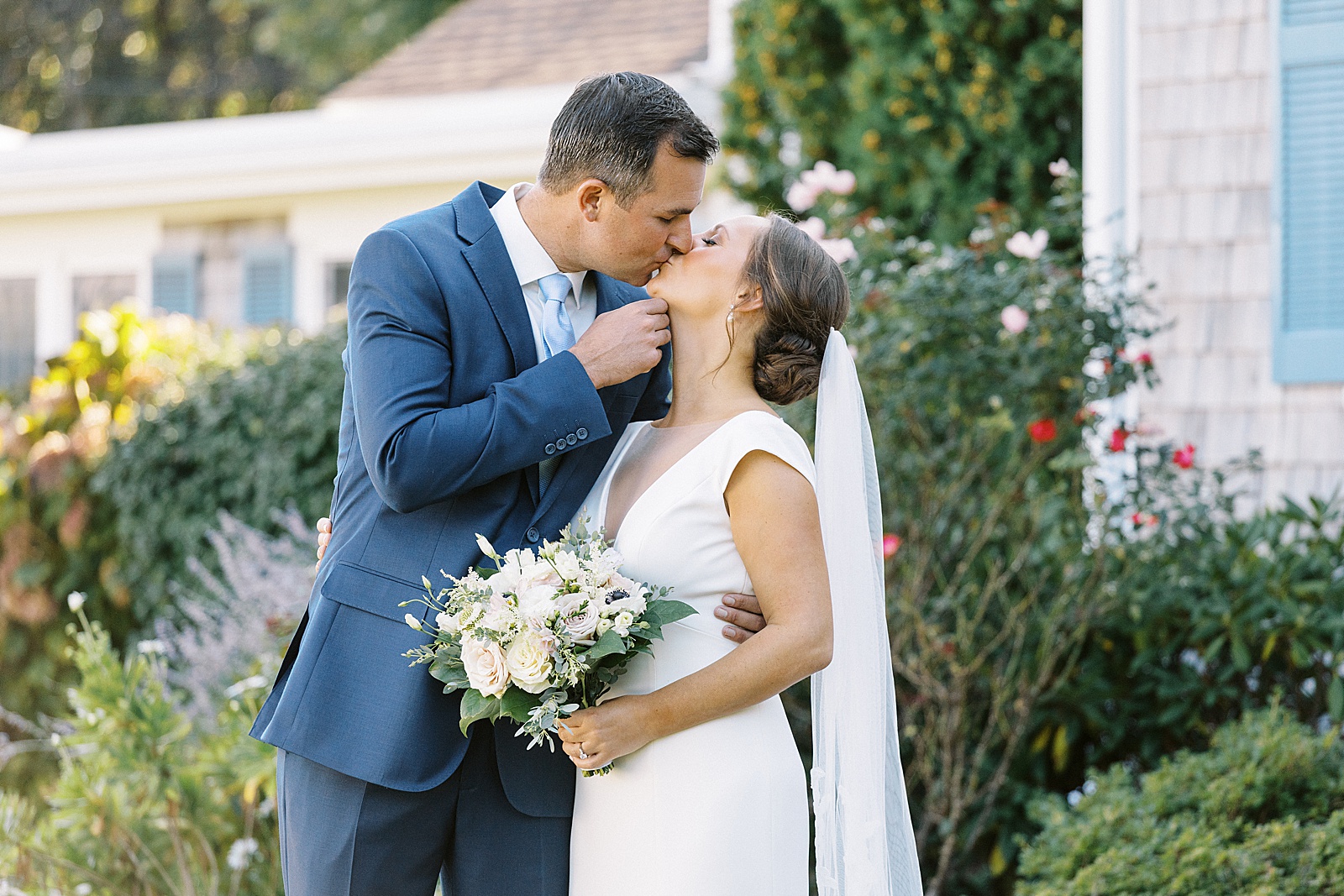 Groom in blue suit kissing bride with white flowers for New York Wedding