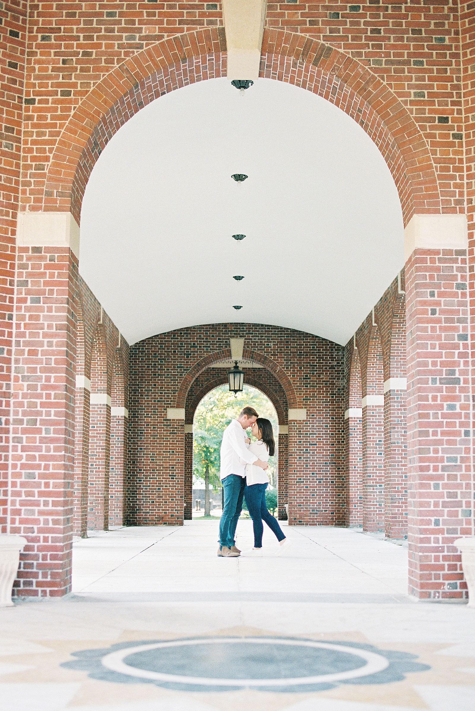 Couple embracing in the archway of a red brick hallway for photo shoot 