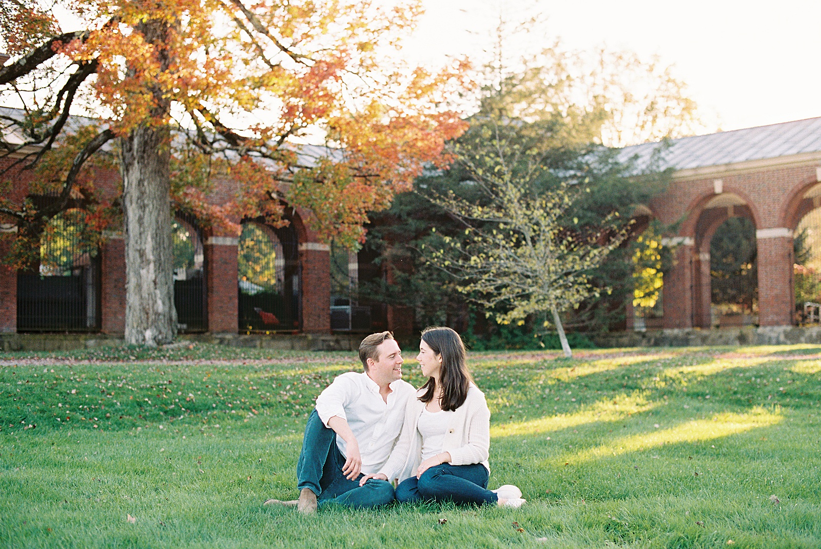 Couple wearing white and denim sitting on a lawn together for engagement photo shoot 