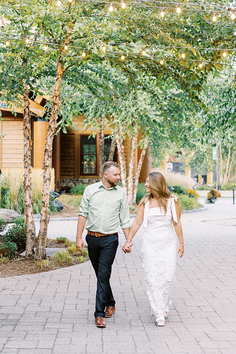 engaged couple walk under twinkle lights by Lynne reznick photography