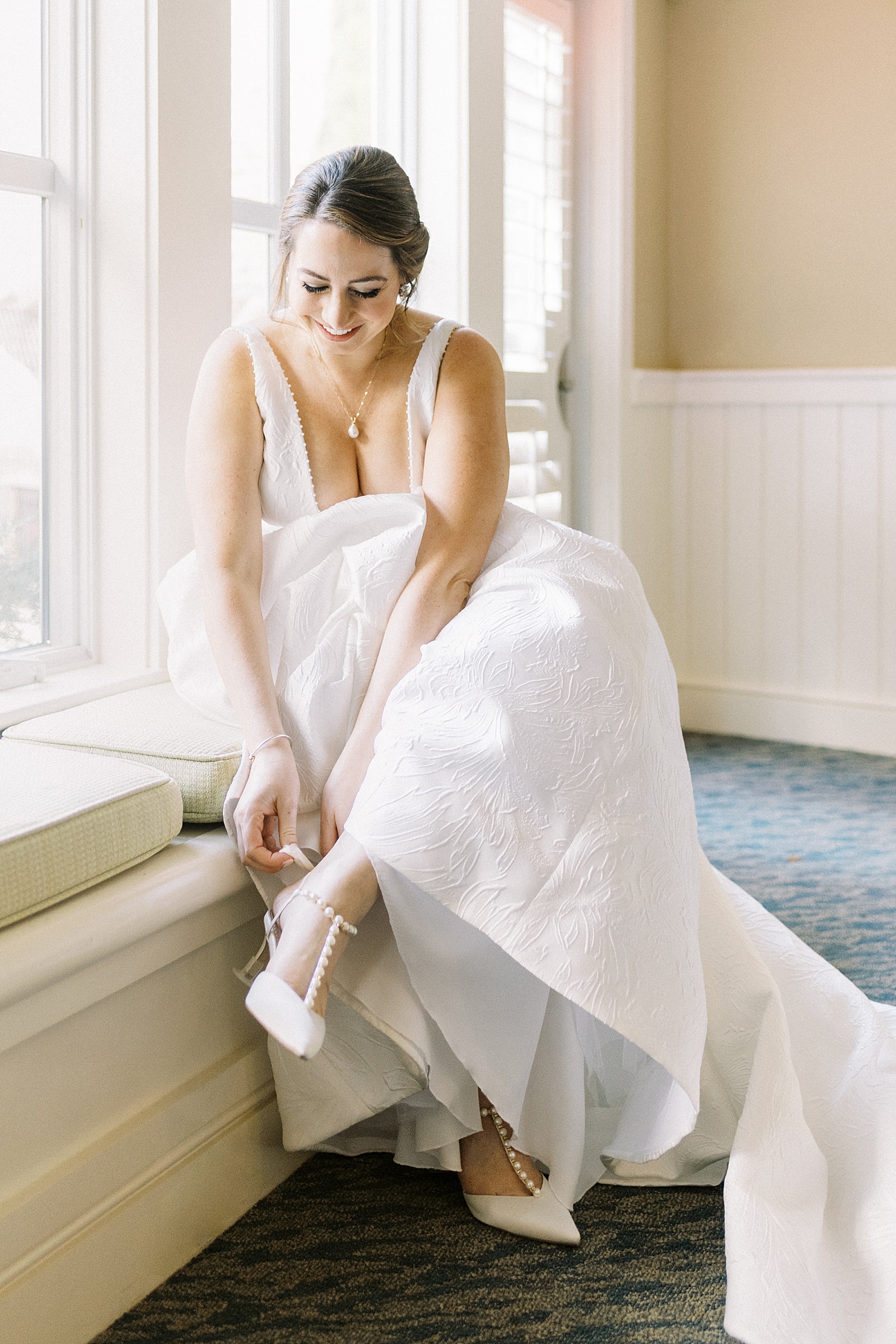 Bride putting on her shoes in a window seat 