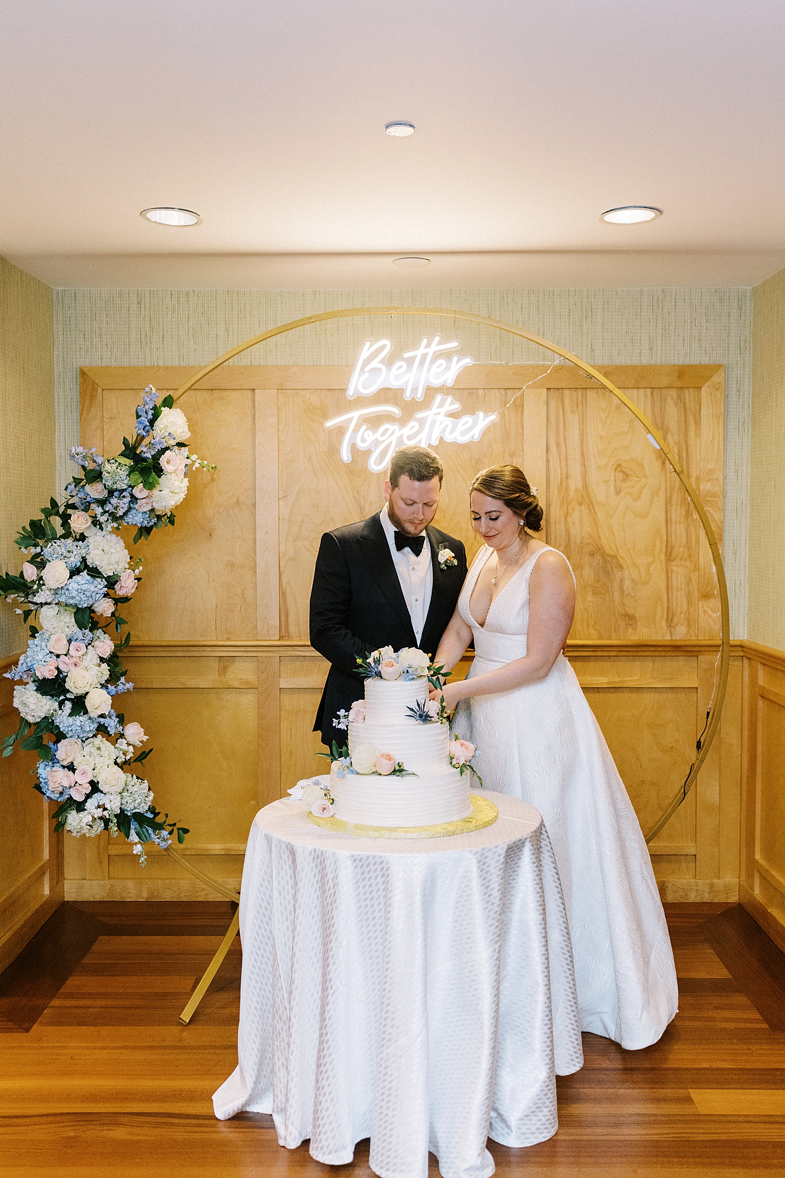 Newlyweds cutting a cake in front of gold arch and neon sign