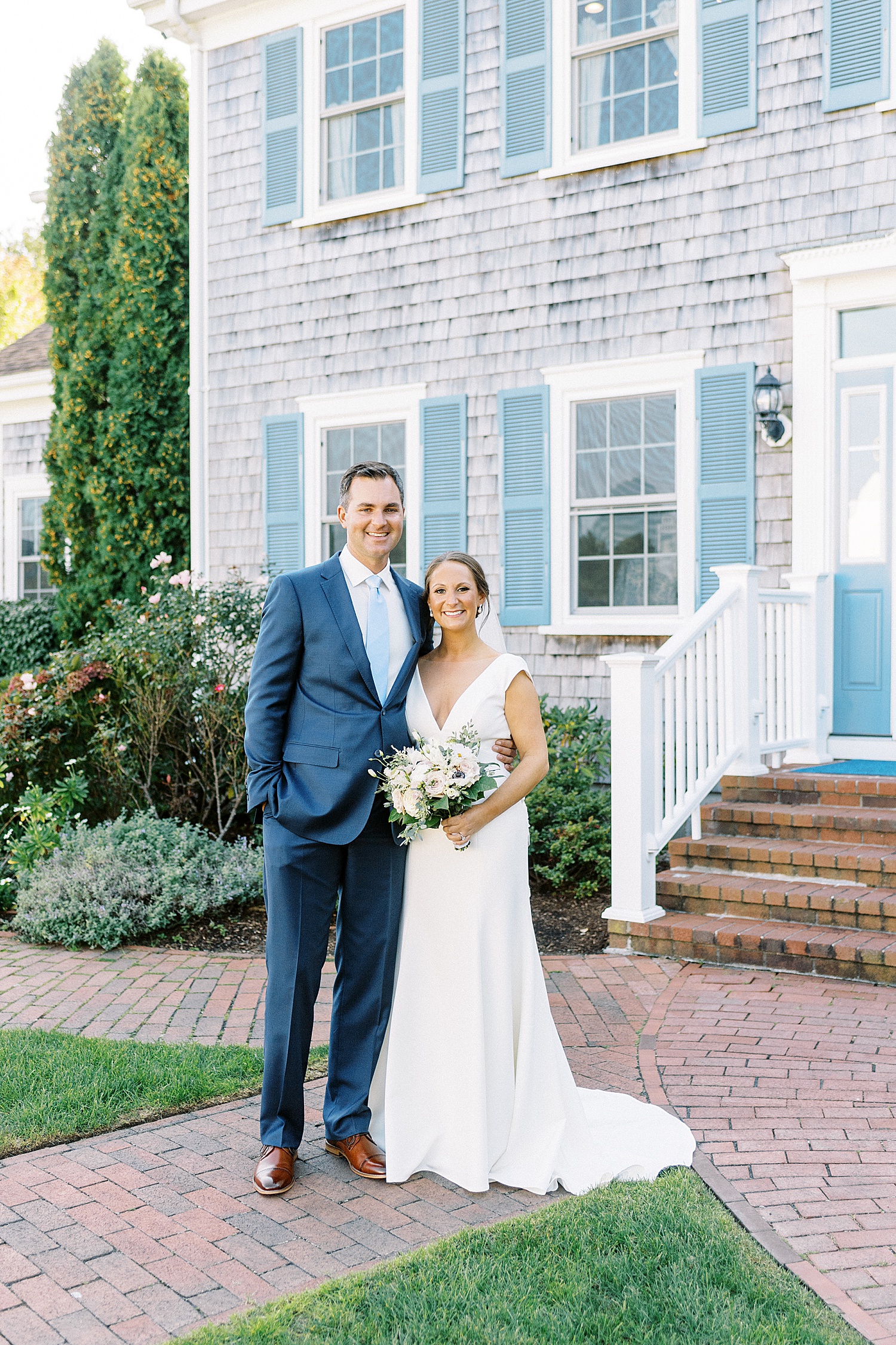 Bride and groom in front of blue house at their Dennis Inn Wedding
