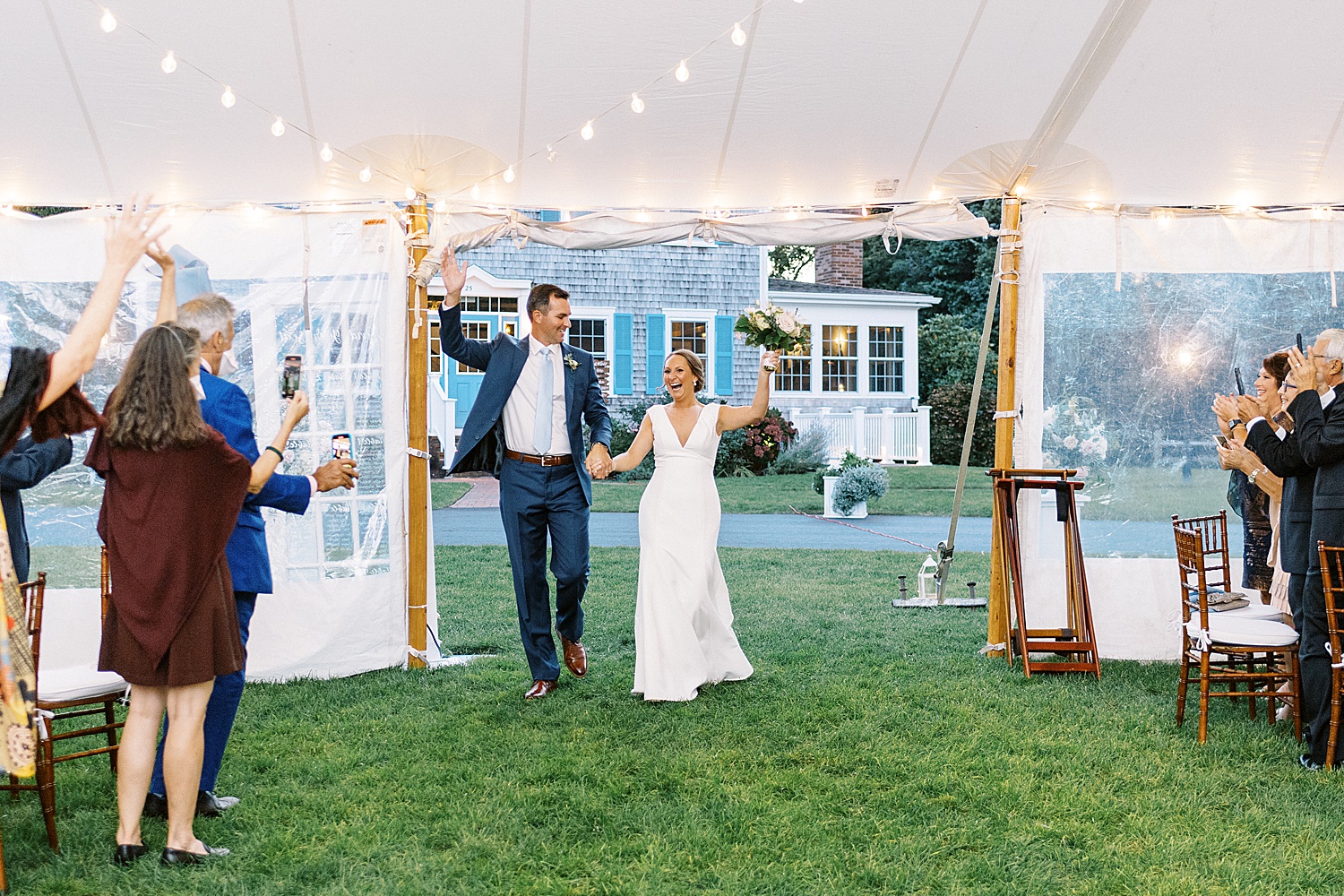 Newlyweds enter their reception under a tent on a lawn
