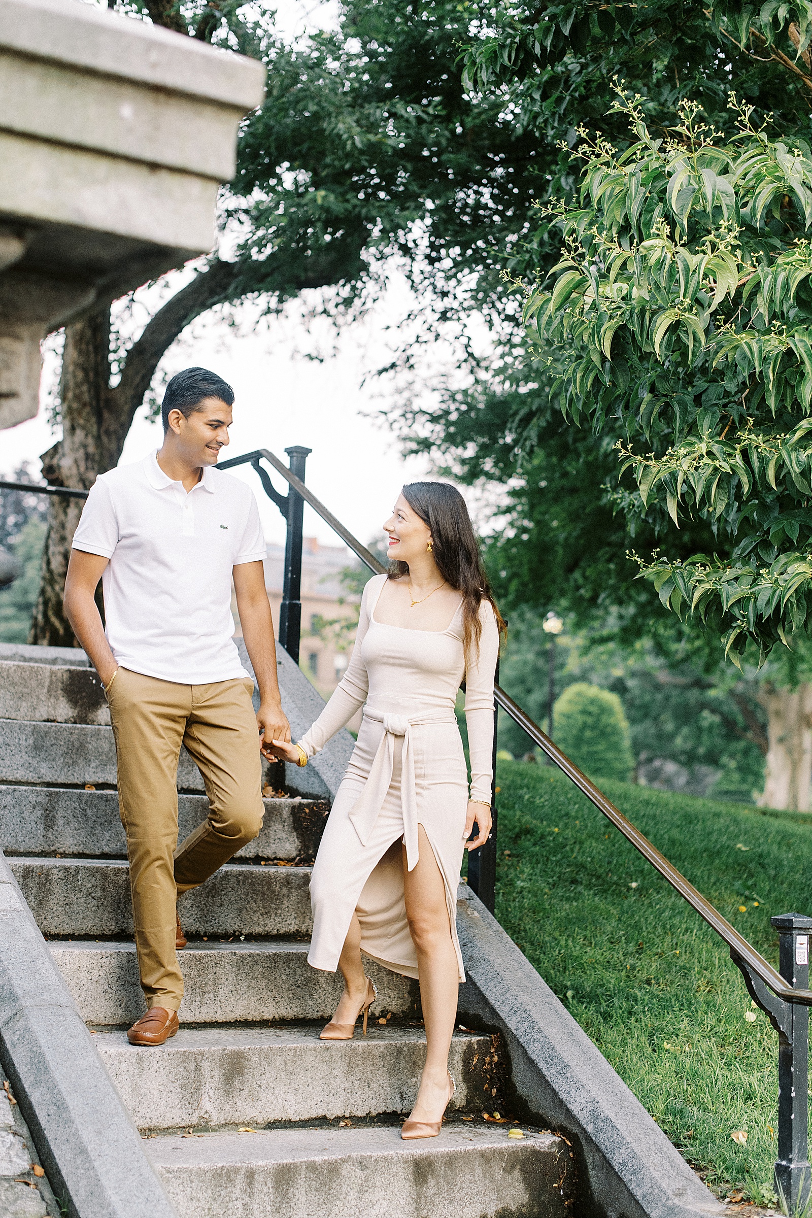 Engaged couple in neutral outfits on stairs by Boston wedding photographer