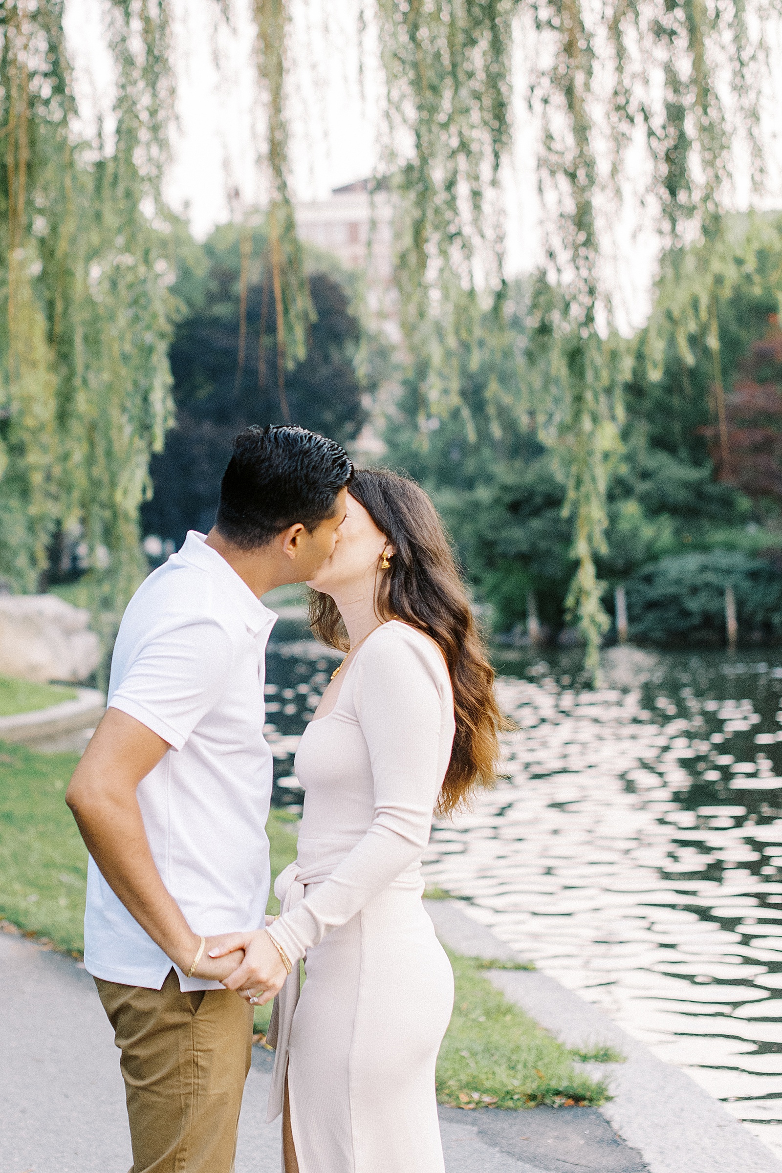 Man and woman kissing next to pond at public garden engagement session