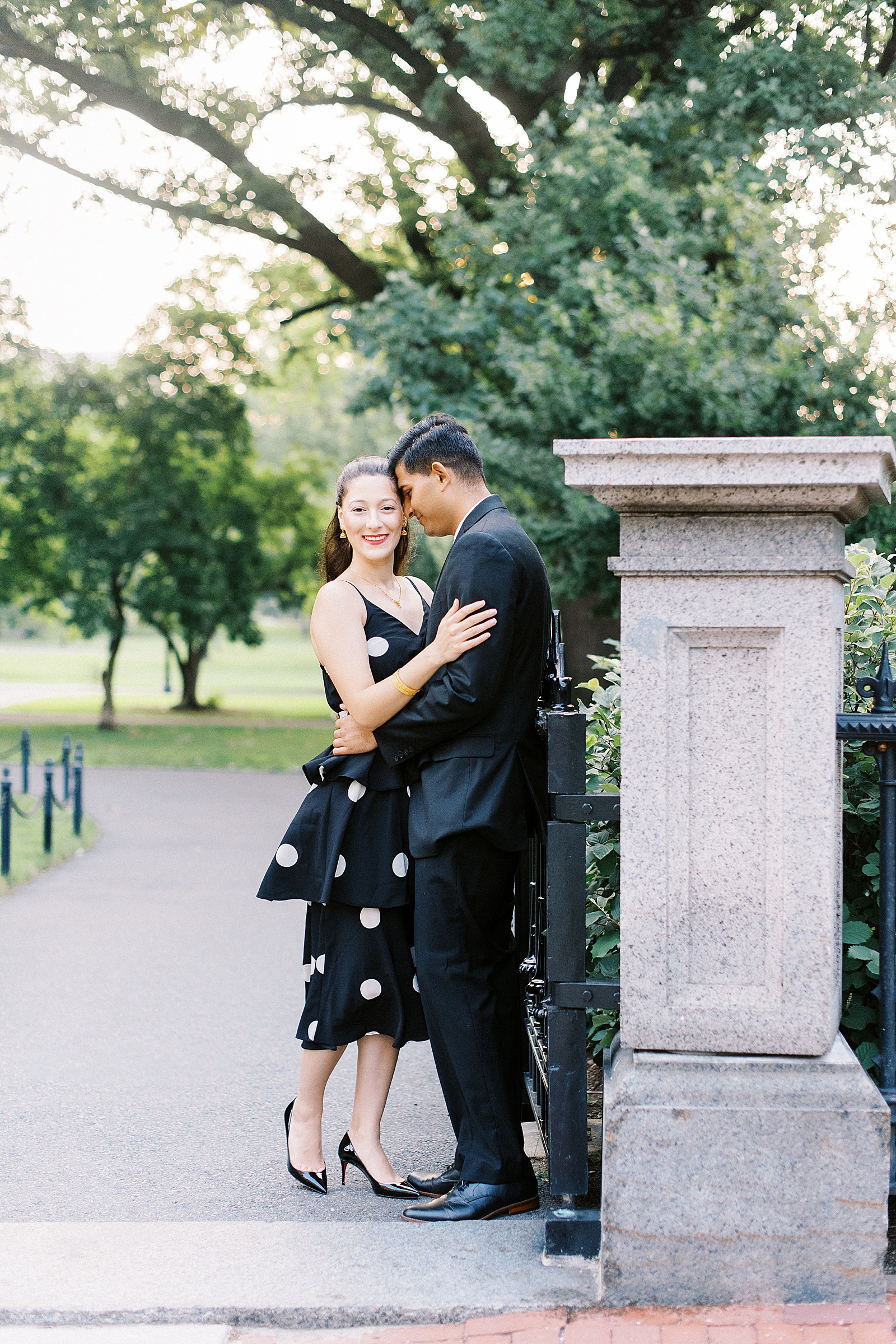 Man leaning into woman next to park gate by Boston wedding photographer