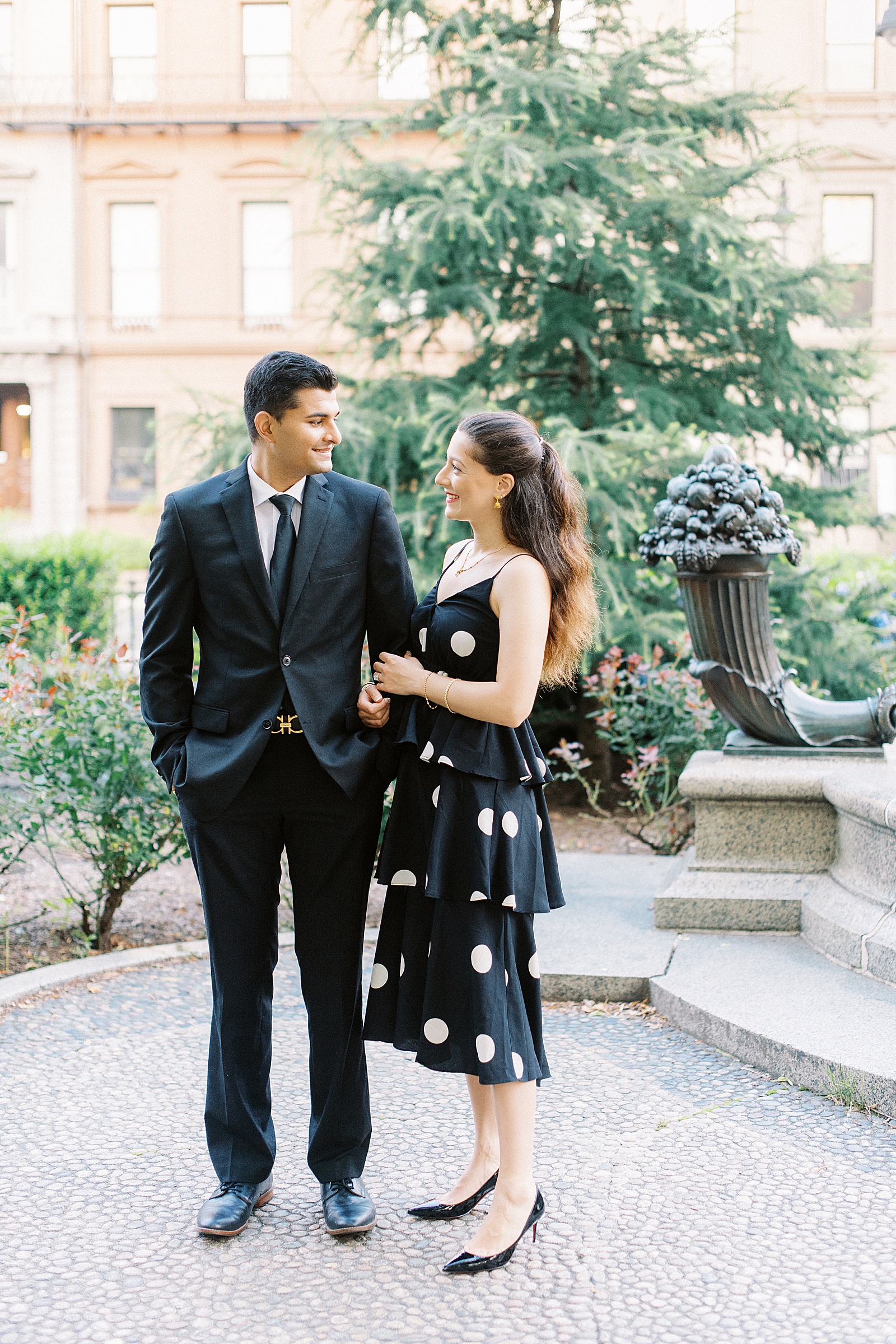 Woman in polka dot dress and man in suit for public garden engagement session