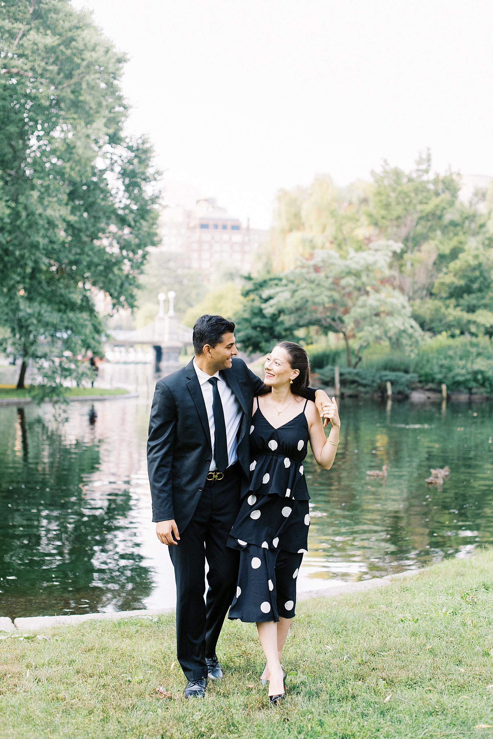 Couple walking arm in arm next to pond for public garden engagement session