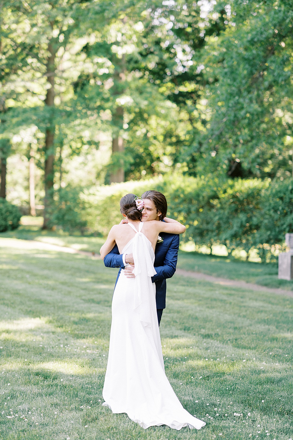 bride in modern elegant gown and groom in blue suit embrace before outdoor Glen Magna farms wedding