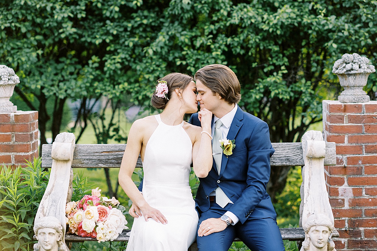 preppy young bride and groom pose on garden bench before ceremony shot by Lynne Reznick Photography