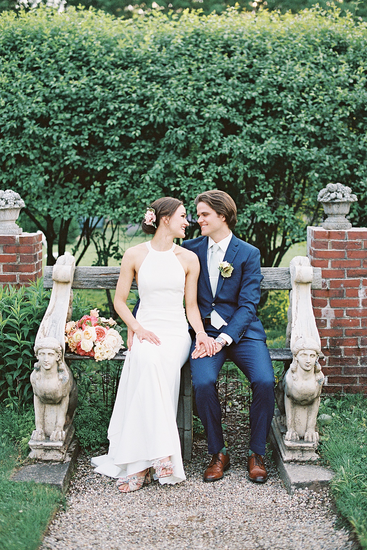 preppy bride and groom in blue suit pose on garden bench before ceremony shot by Massachusetts wedding photographer
