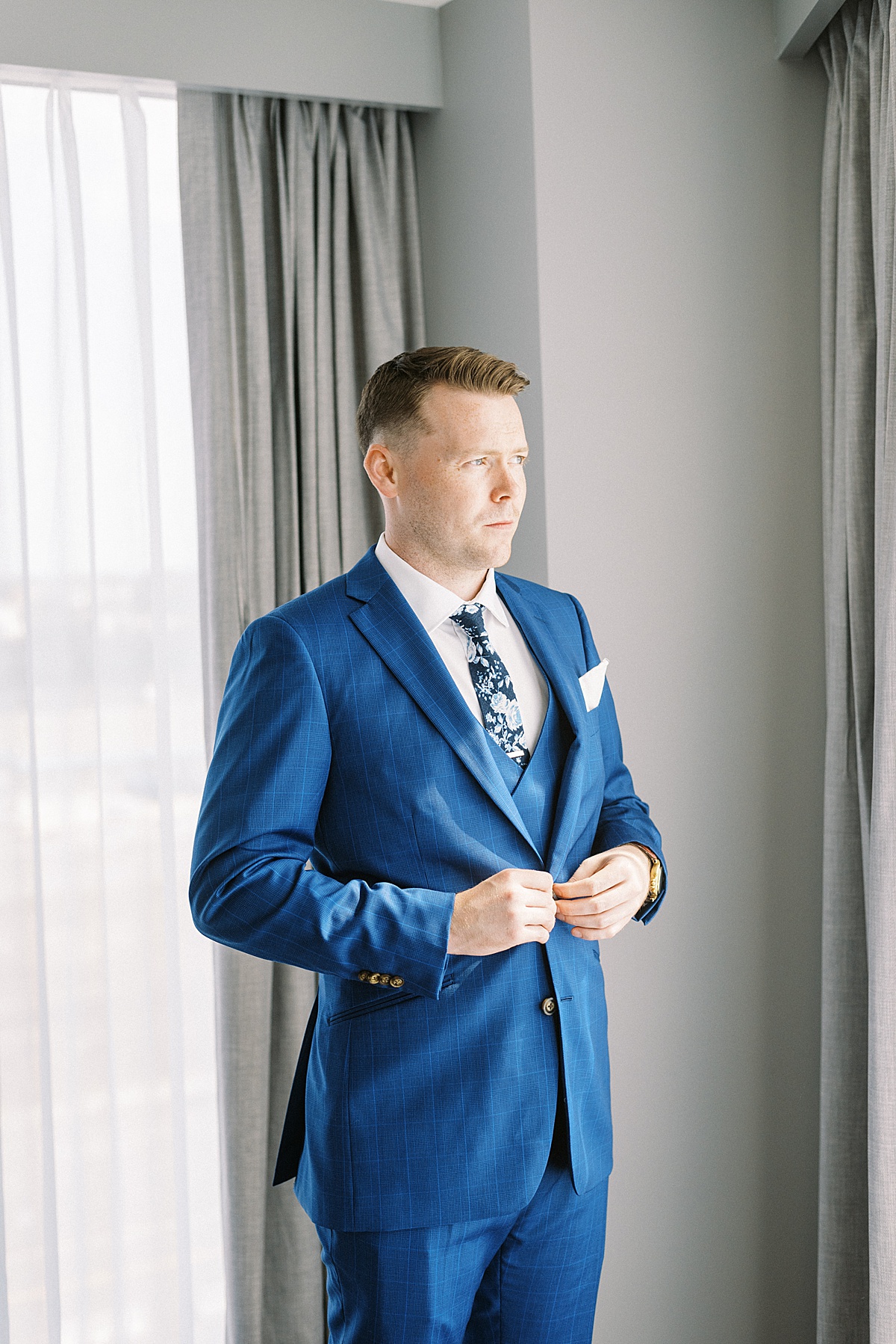 groom in blue suit and floral tie gets ready before nautical oceanview wedding