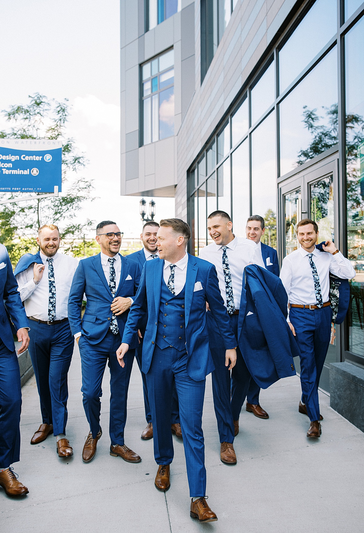 groom and groomsmen in blue three piece suit and floral ties walk Boston pier before nautical oceanview wedding