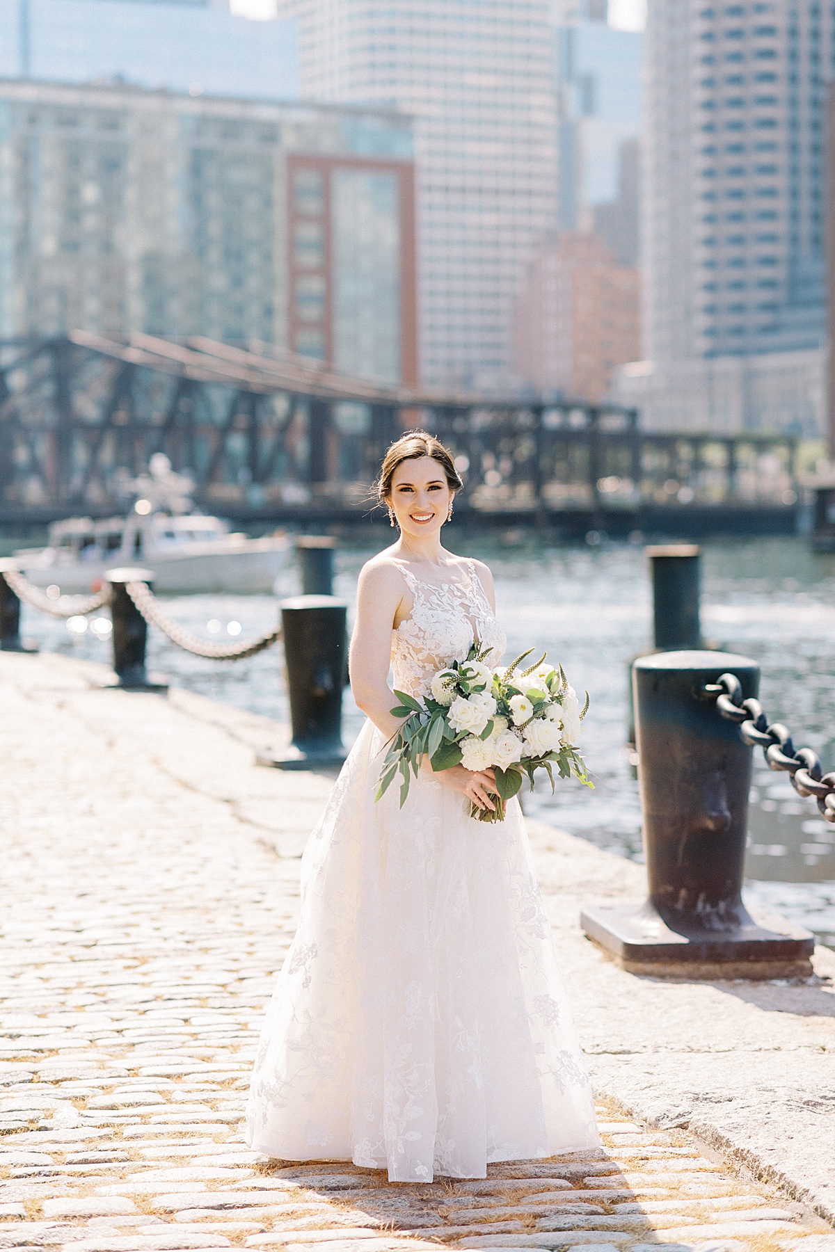 bride in romantic lace gown and white flowers poses on pier for Massachusetts wedding photographer