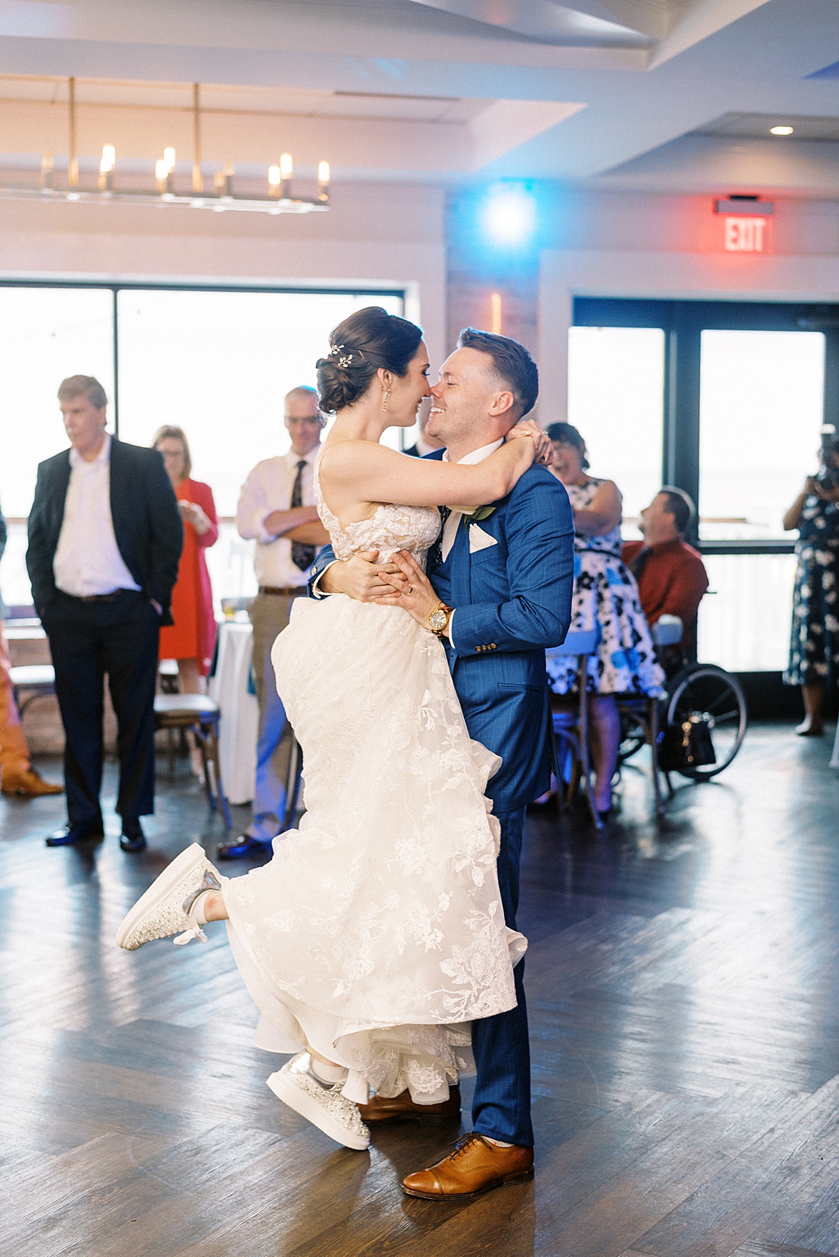 bride in lace gown and sneakers dances with groom in blue tux during first dance at reception shot by Massachusetts wedding photographer