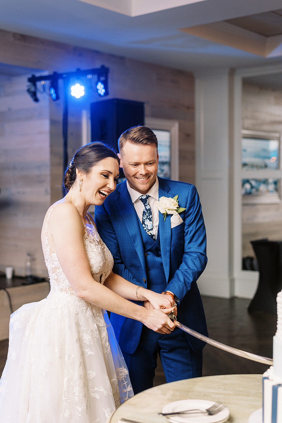 bride in lace gown and broom in blue suit cut cake with a sword after ceremony shot by Massachusetts wedding photographer