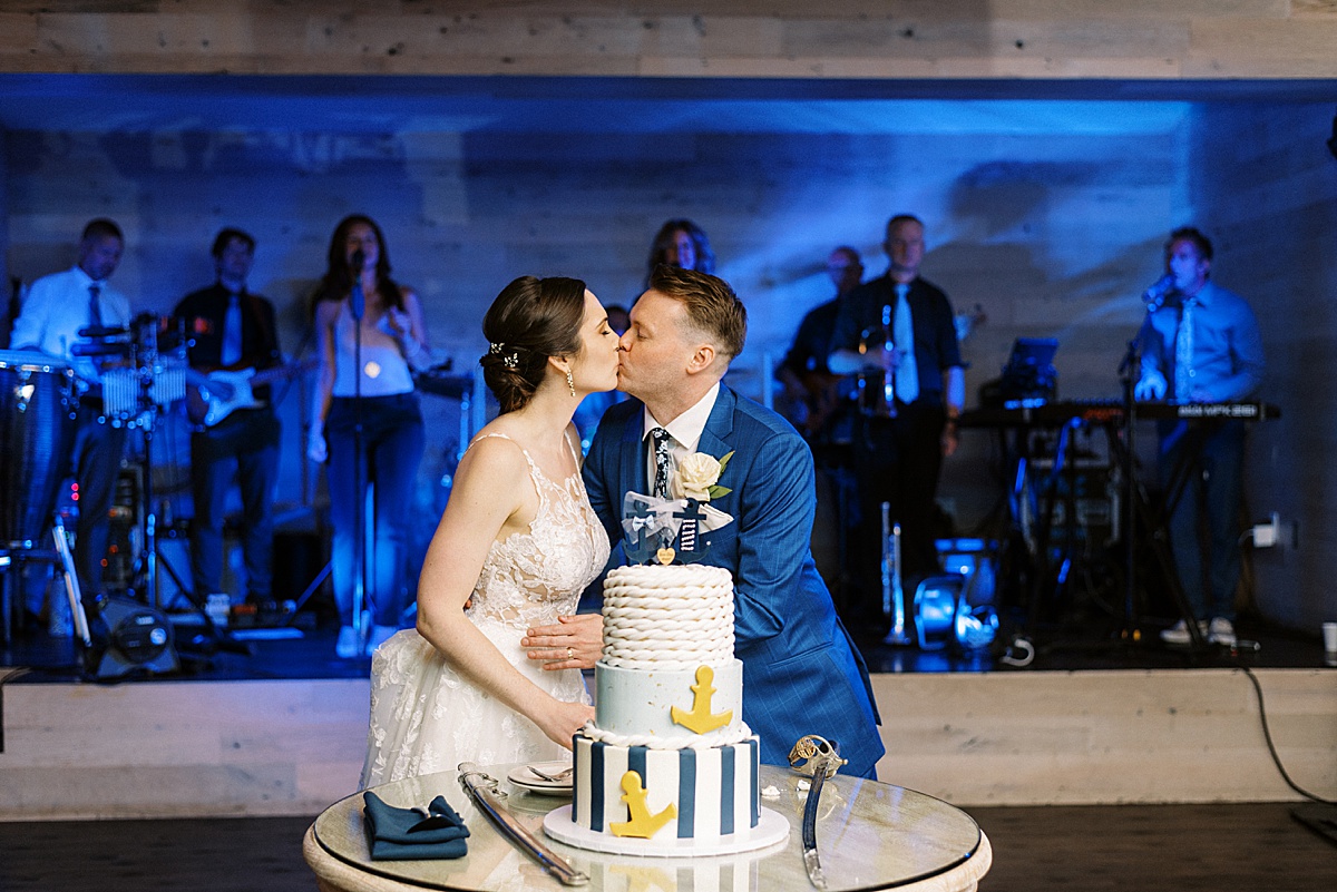 bride and groom kiss next to nautical themed cake at reception shot by Massachusetts wedding photographer