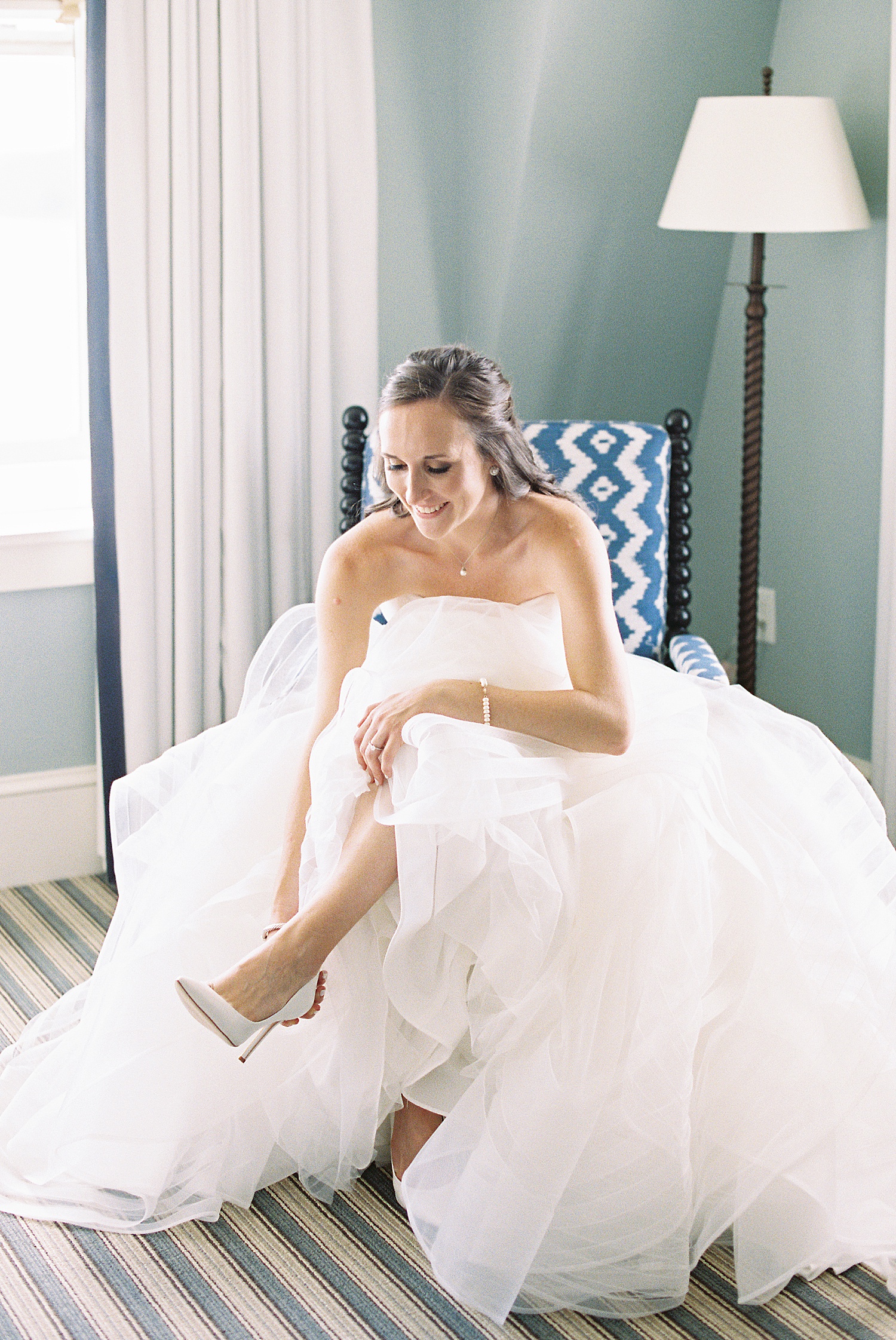 Bride putting on her heels in blue chair by Lynne Reznick photography