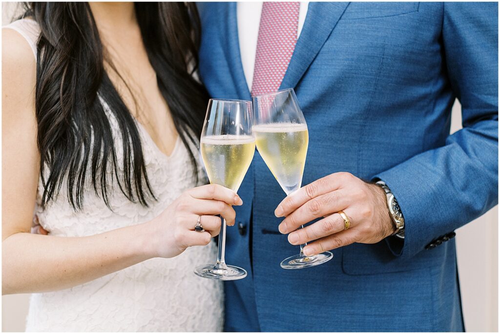 detail of bride and groom hands clinking champagne flutes