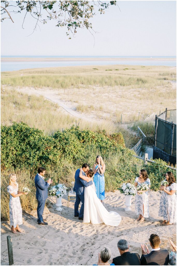 newlyweds first kiss with views of the beach and ocean in the background during cape cod wedding weekend