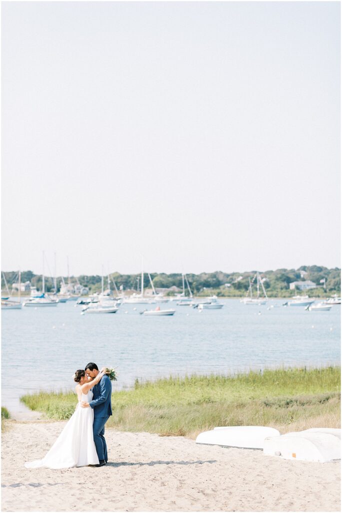 couple poses in front of harbor dotted with boats for Cape Cod wedding weekend