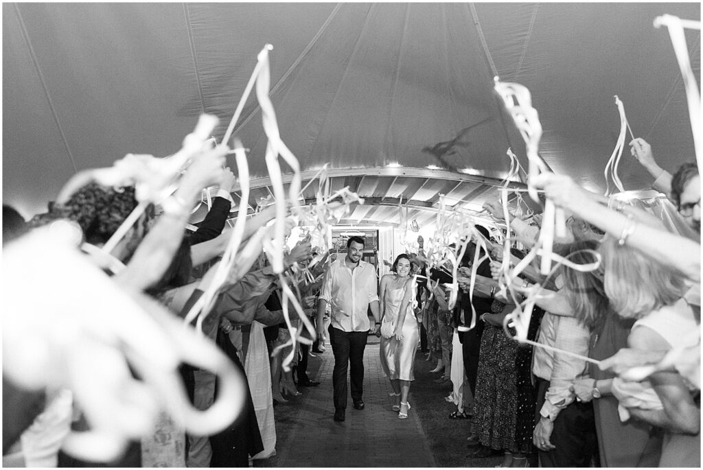 black and white of newlyweds exiting tent with streamers blowing 