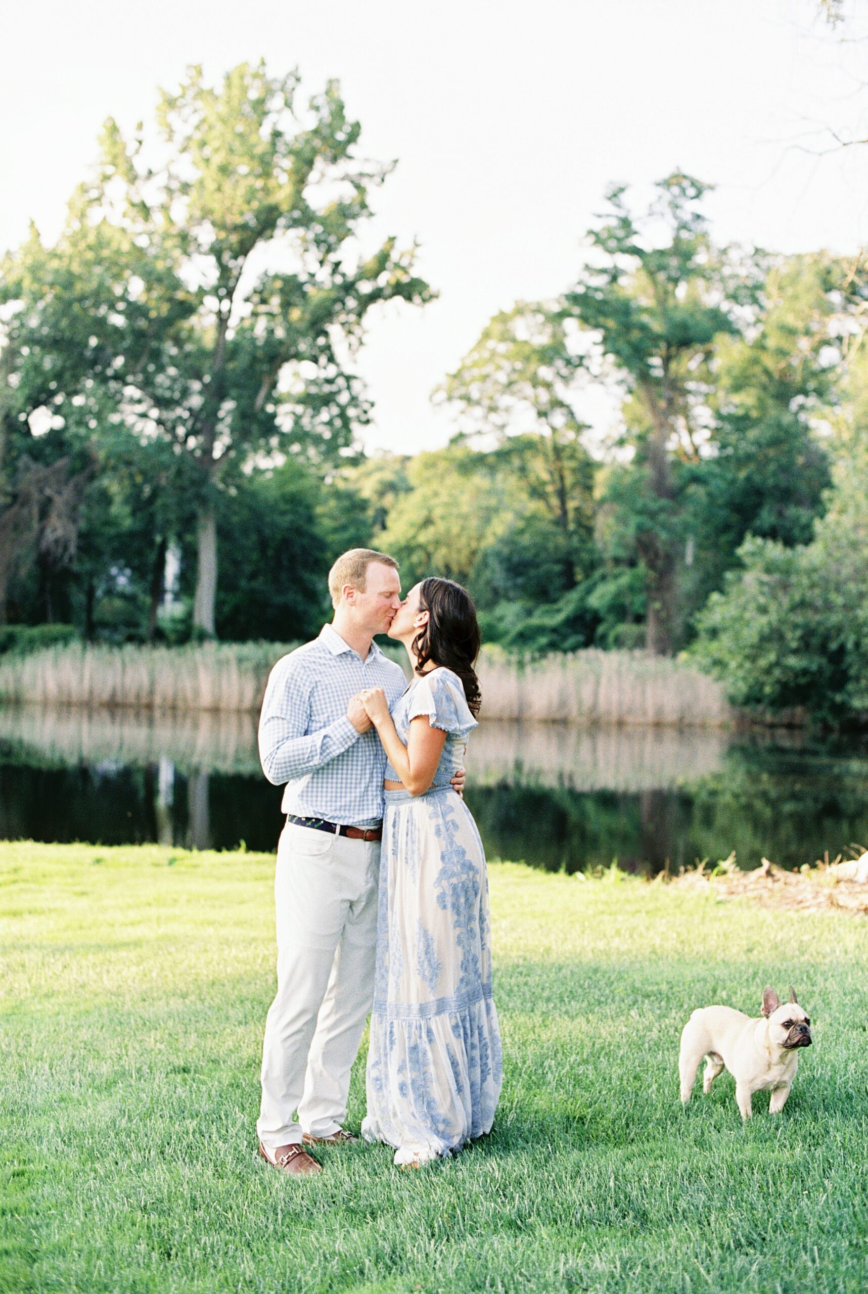 couple in blue and white outfits with frenchie pose on golf course for their engagement session with Boston wedding photographer Lynne Reznick