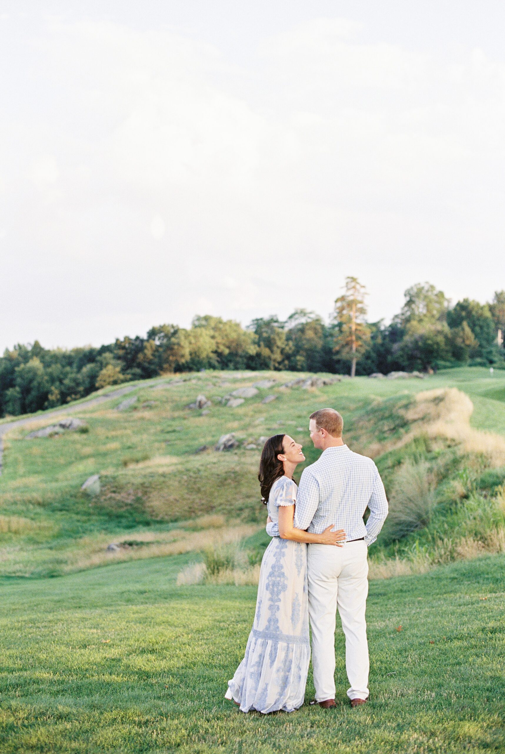 coouple walking along fairway in french blue outfits during golf course engagement session in NY with Boston wedding photographer Lynne Reznick