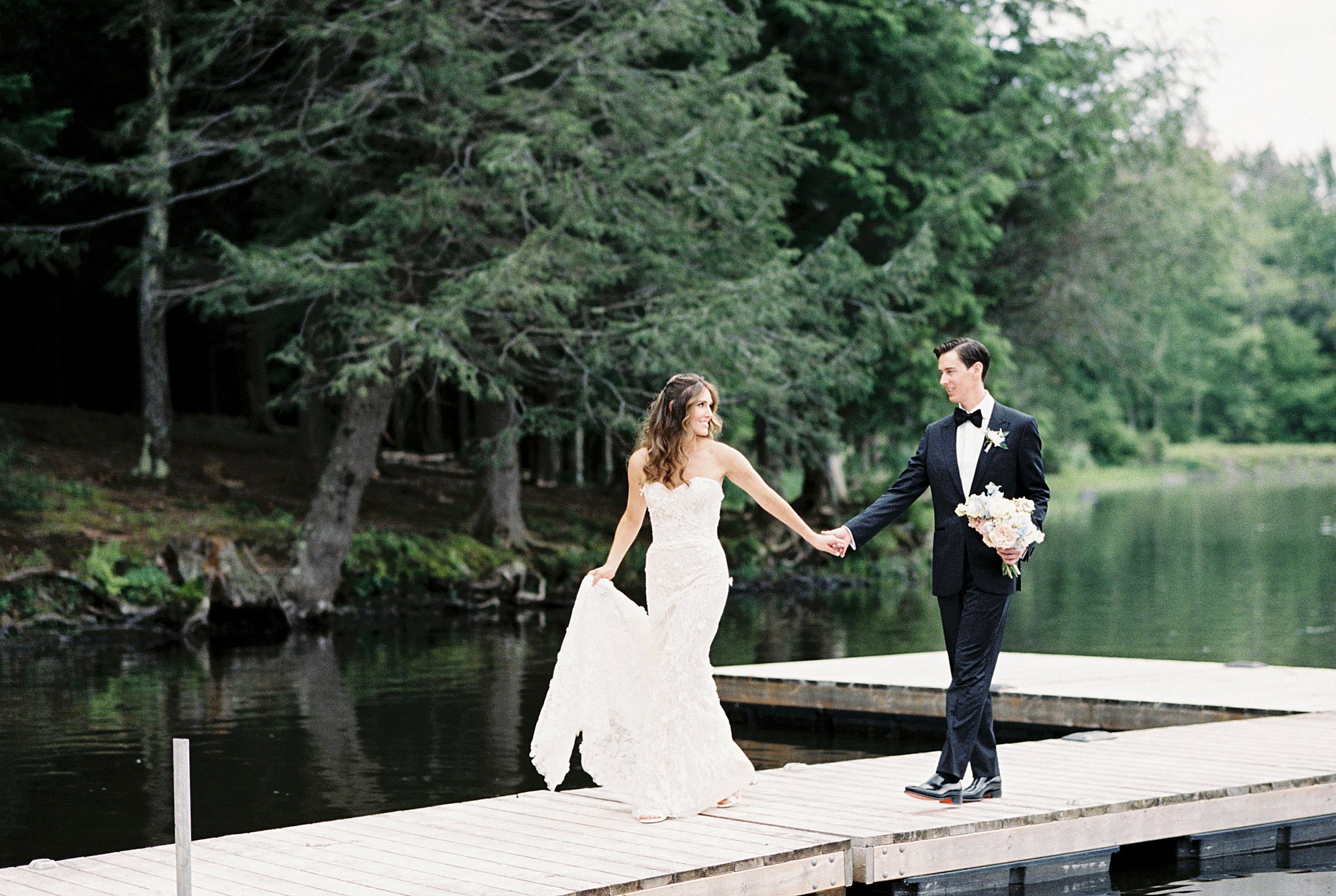 newlyweds walk along dock holding hands and looking at each other by Lynne Reznick Photography 