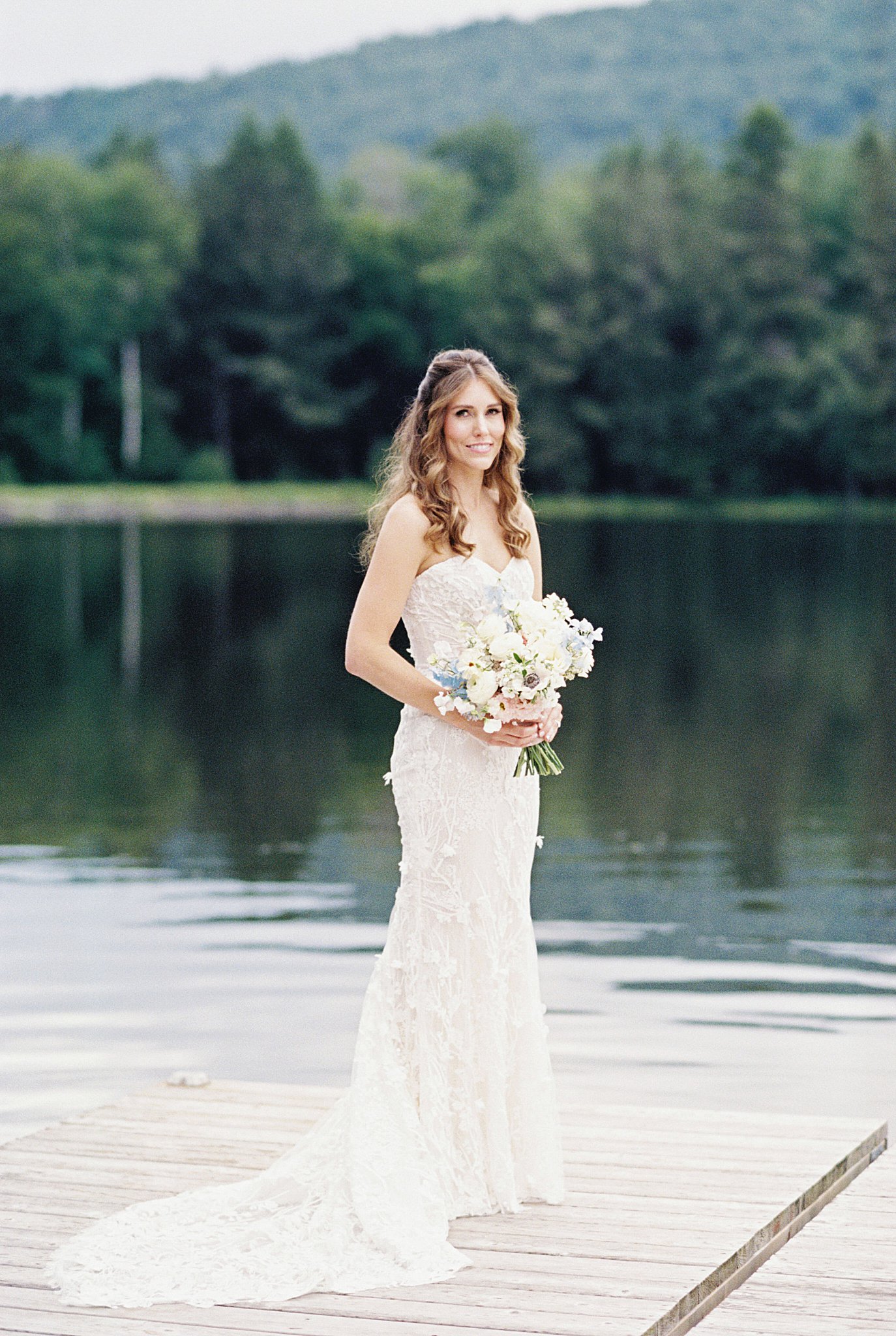 bride's train flows around her ankles as she holds bouquet in front of lake at Onteora Club