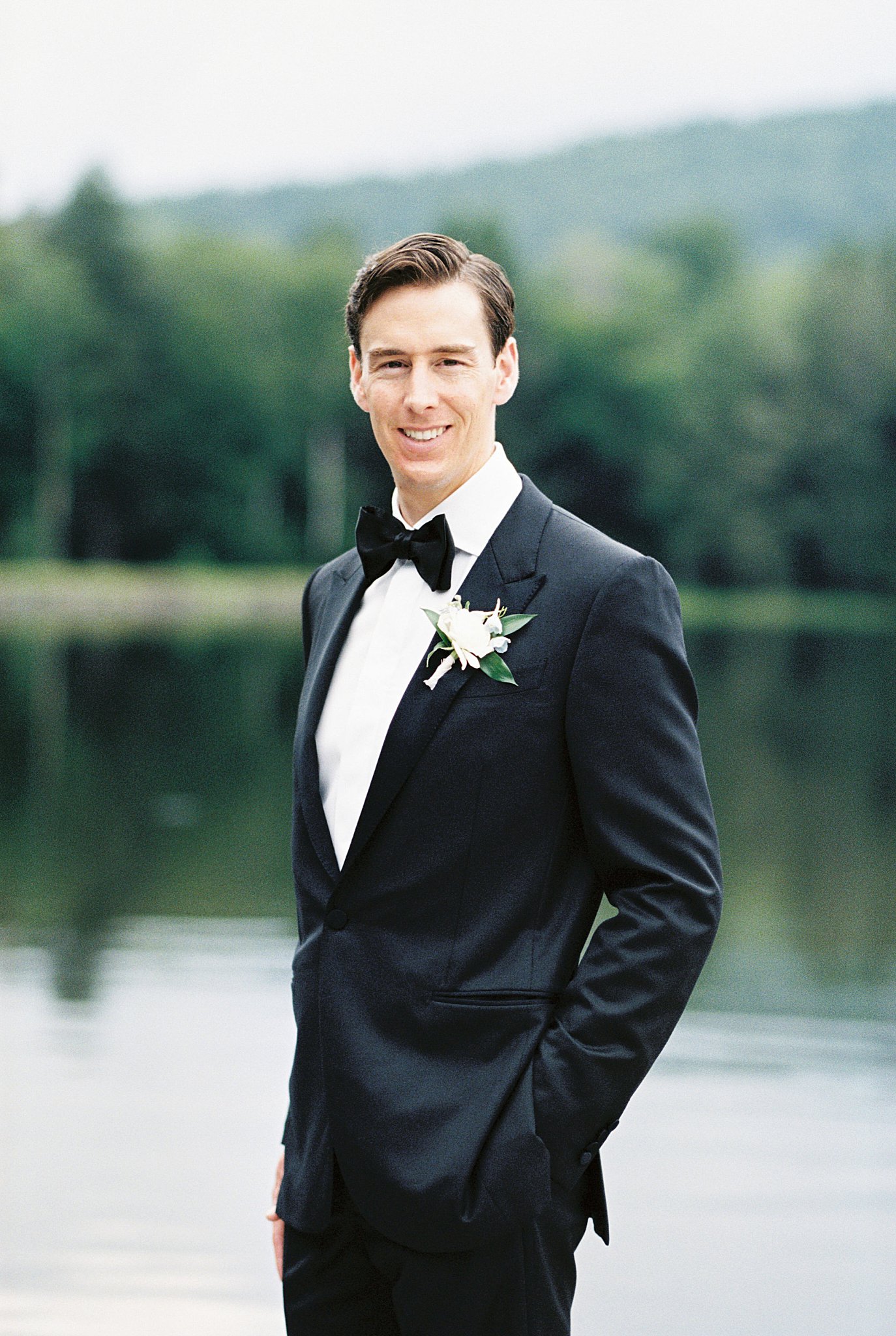 groom tucks hands in pocket as he stands on dock by Cape Cod wedding photographer