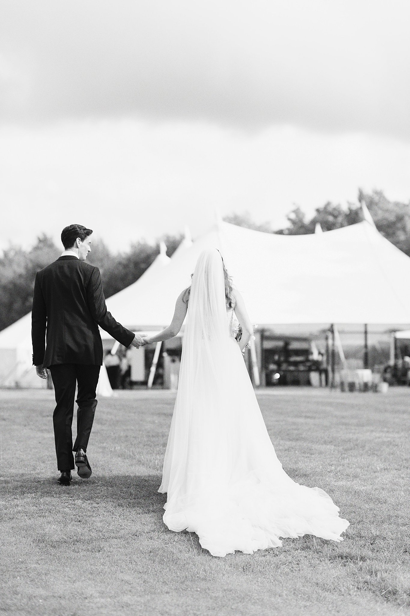 man holds bride's hand as they walk toward tented reception by Catskills wedding photographer