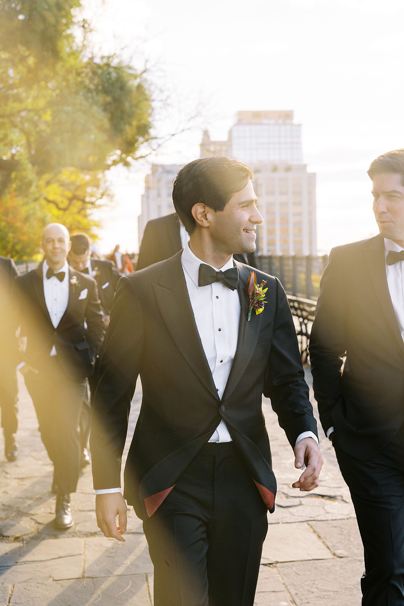 sun shines through on groom walking by NYC wedding photographer 