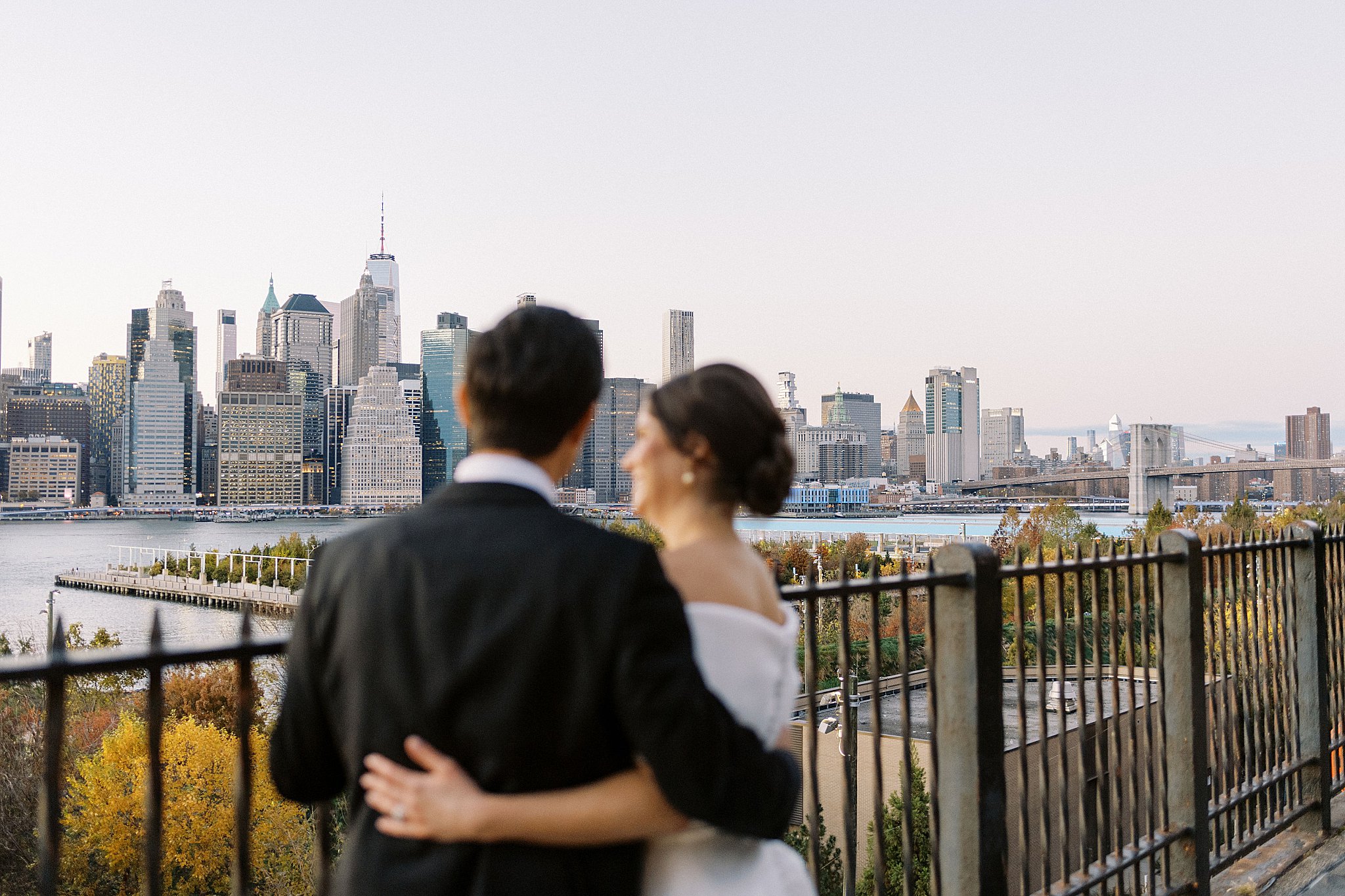 man and woman put arms around each other in front of skyline by NYC wedding photographer 