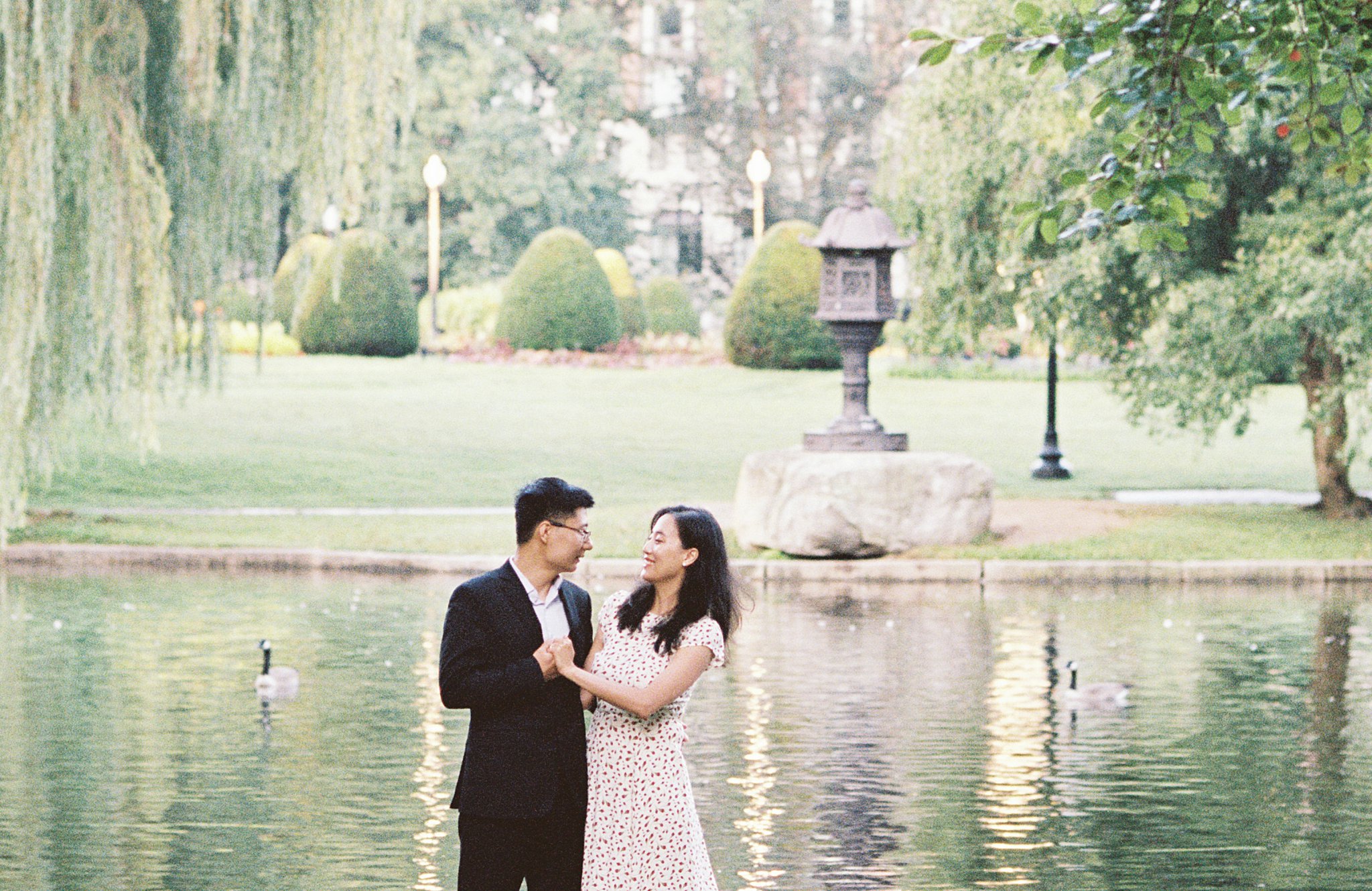 man holds woman's hand as they look at each other in front of a pond at Public Garden Anniversary session
